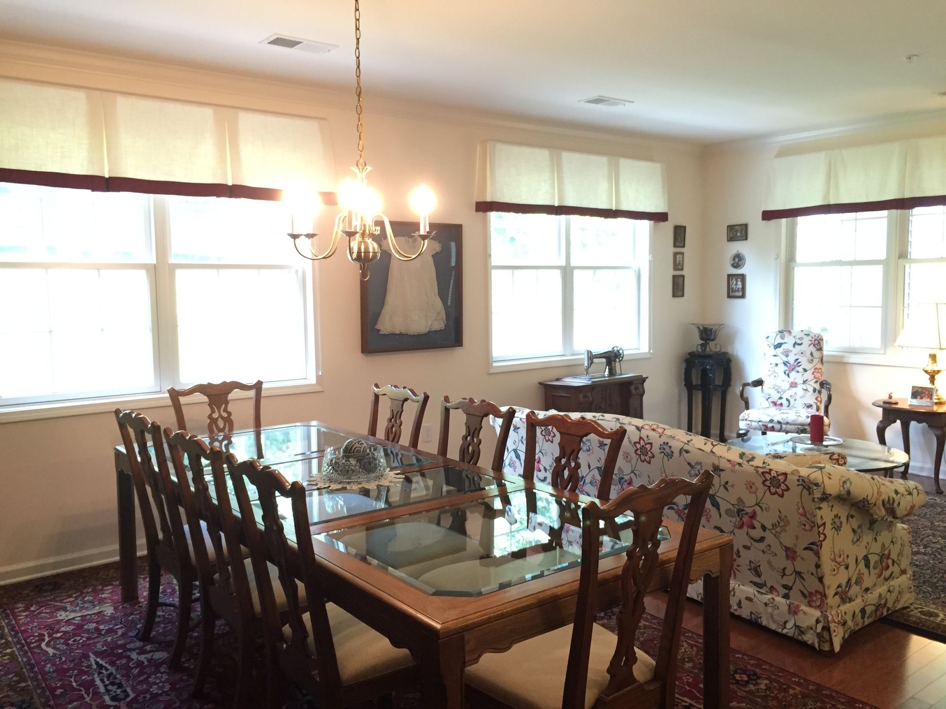 Formal dining room with long table, chairs, and windows with beige and burgundy trim.
