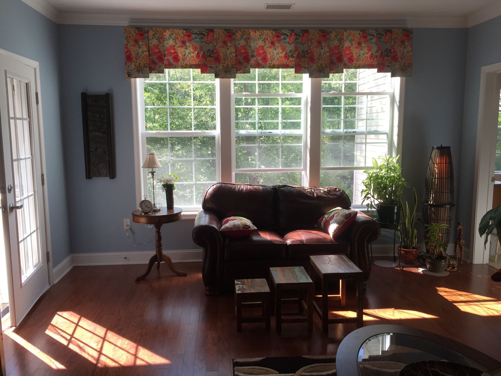 Living room with a brown leather sofa, three windows, and wood flooring.