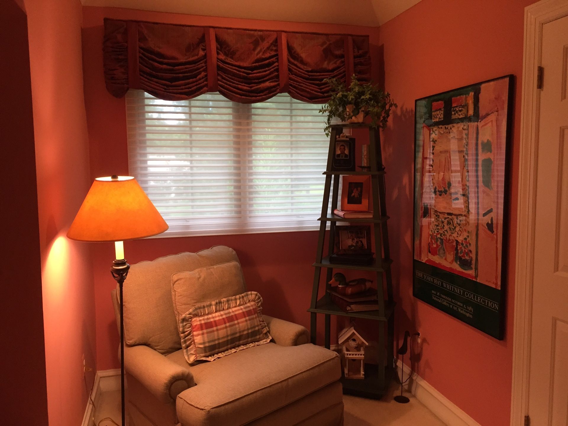 A cozy reading nook with a chair, lamp, window, and shelves in a room painted coral.