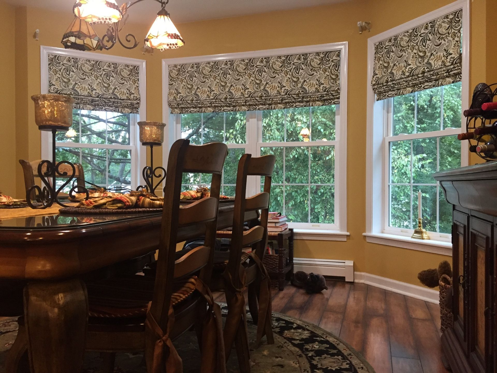 Dining room with a dark wood table, floral window shades, and outdoor view.