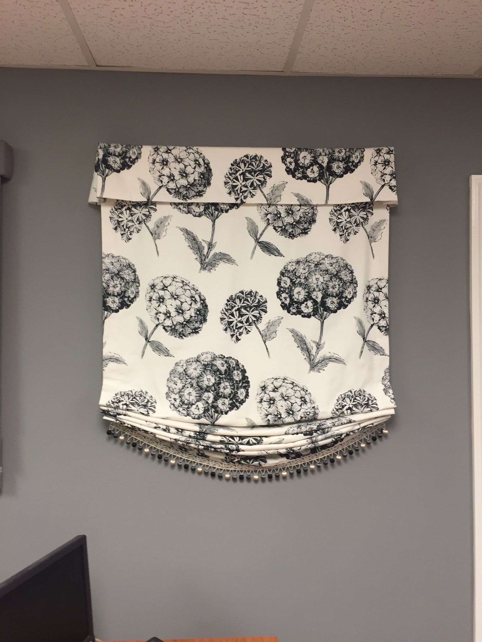 Window shade with black and white floral pattern, gray wall, and beaded trim.