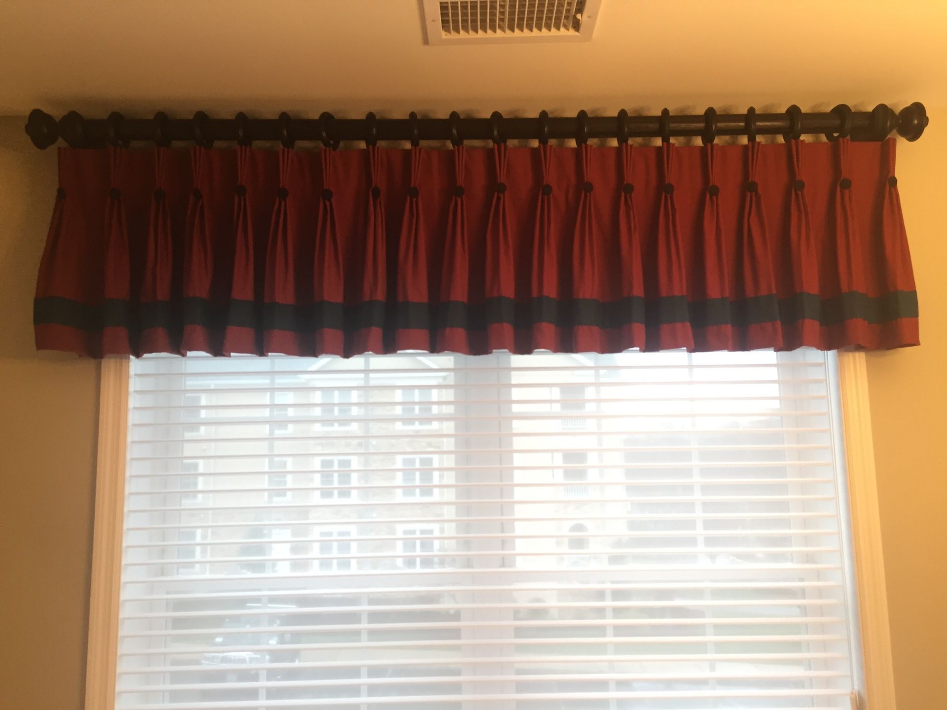 Burgundy and navy window valance over a window with white blinds. Black curtain rod.