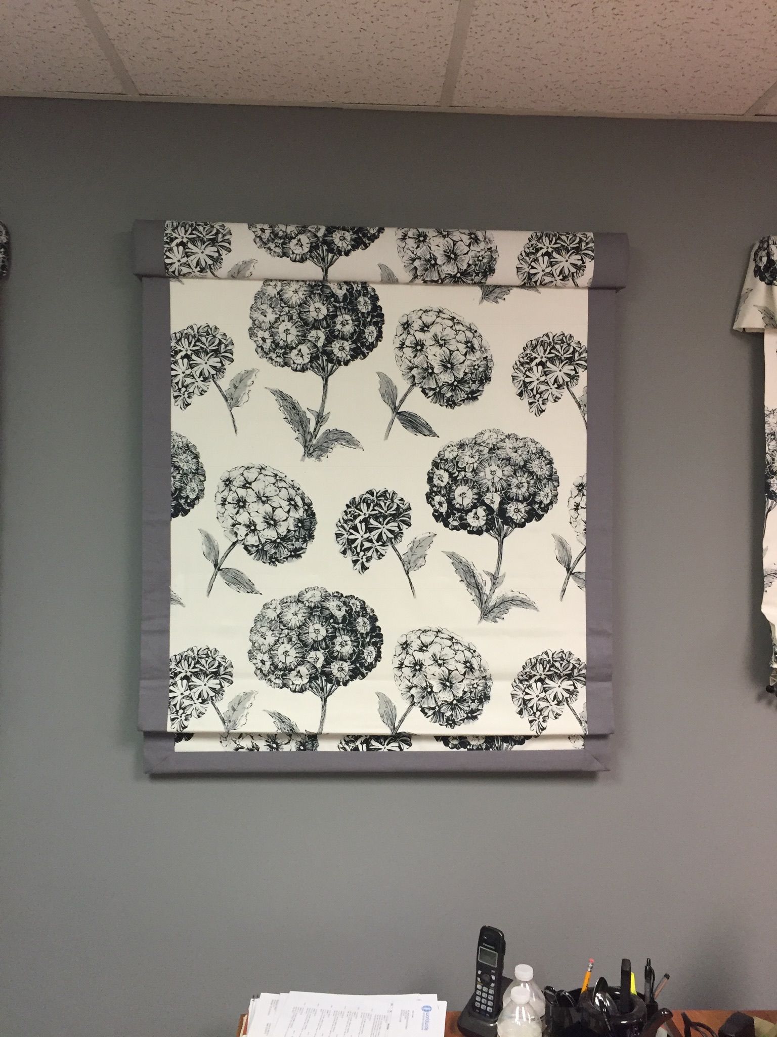 Roman shade with black and white floral pattern on a gray wall.