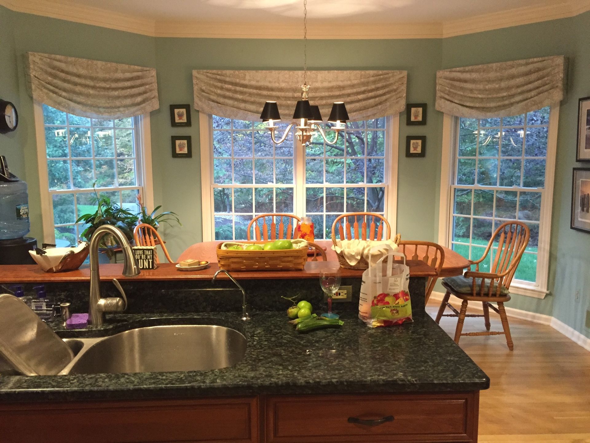 Kitchen with a dark counter, sink, and seated area with windows, wooden table and chairs.