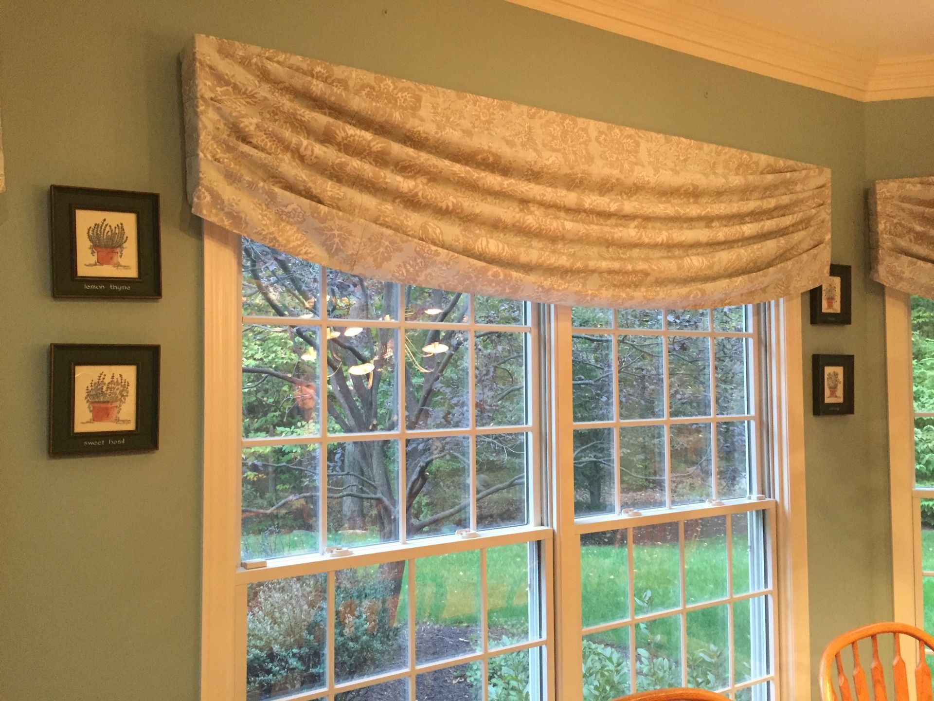 Window with decorative fabric valance, framed artwork on a green wall.