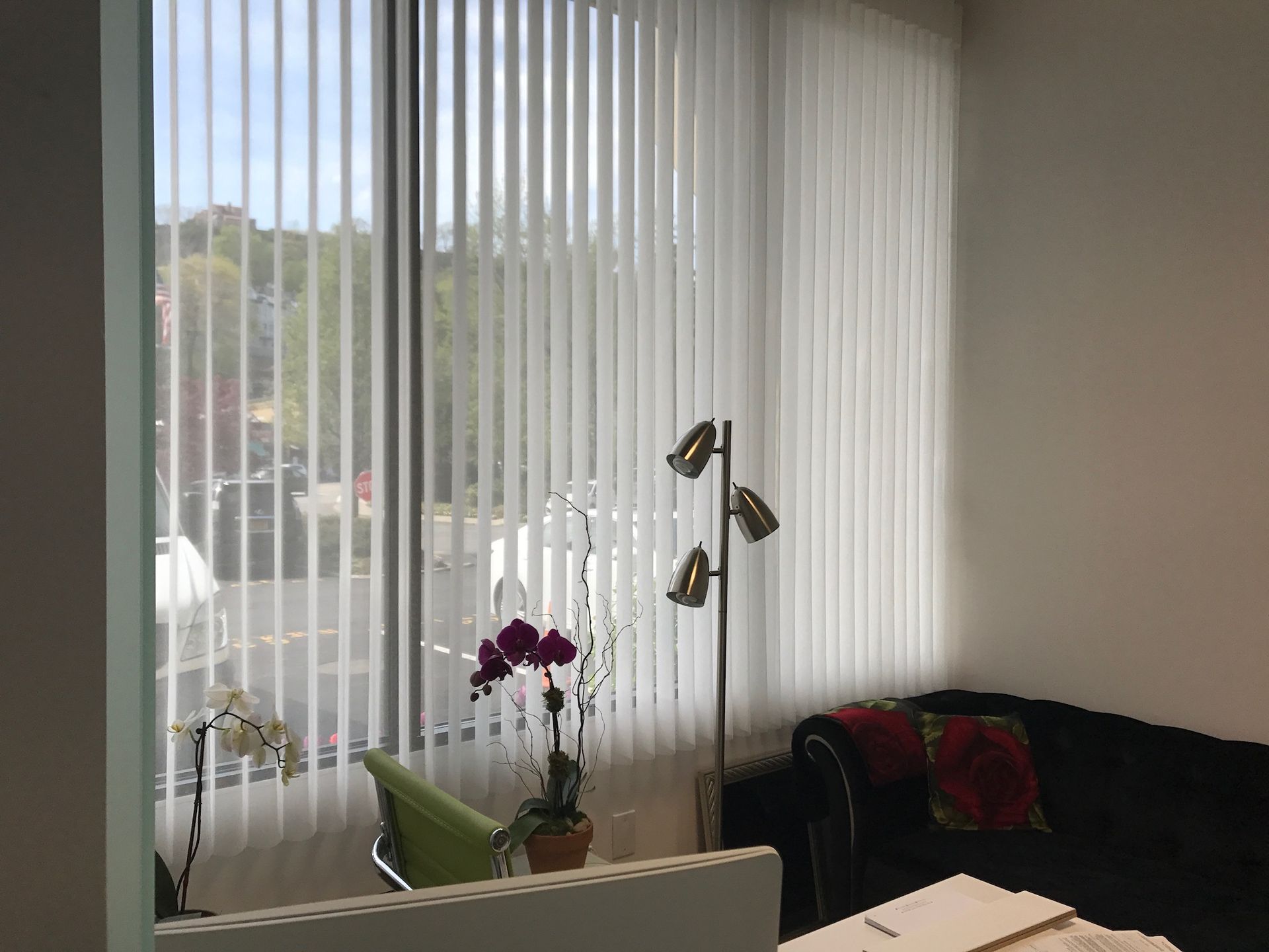 Vertical blinds on a window, next to a couch, lamp, and plant.