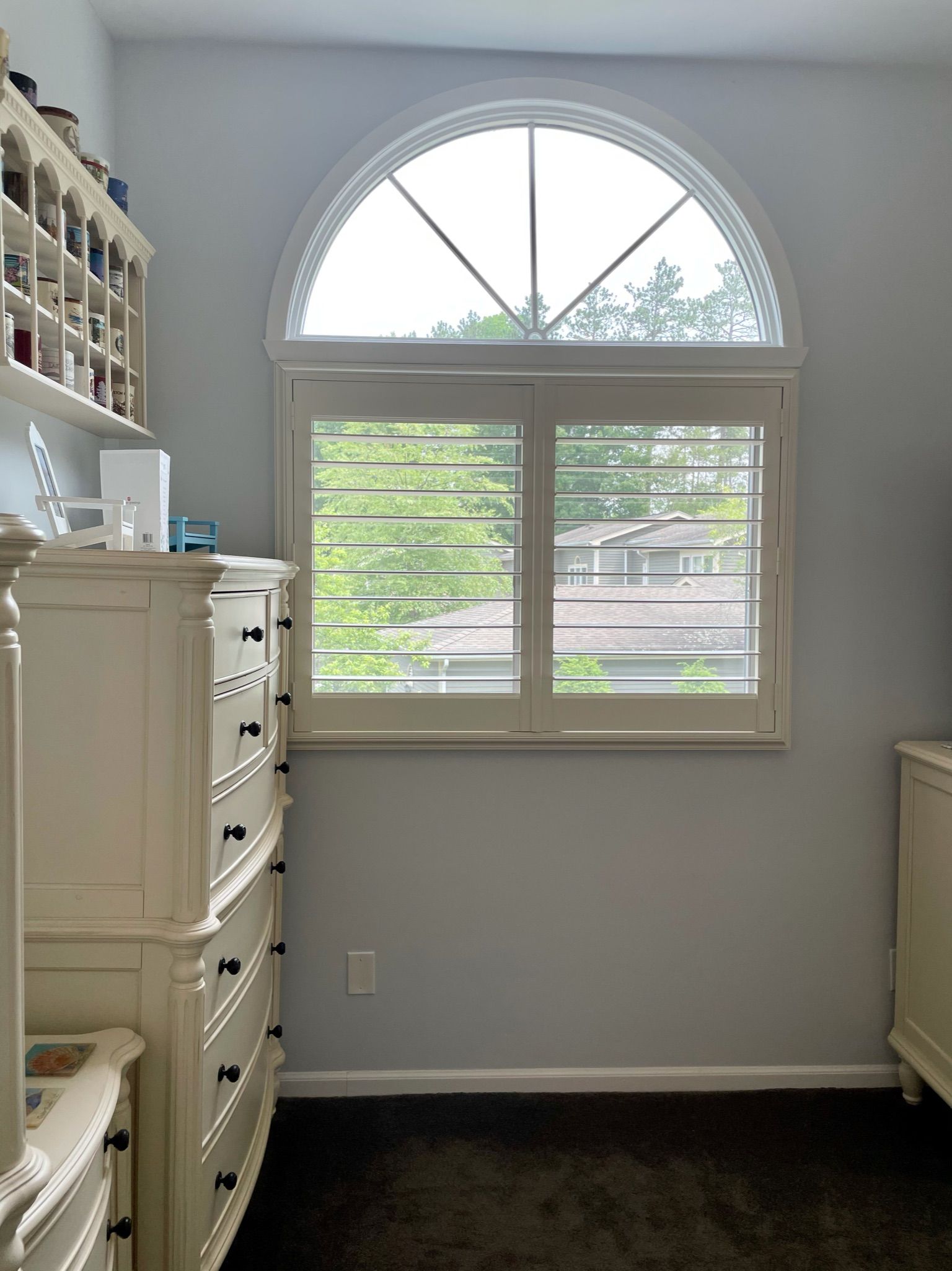 Bedroom with a white arched window, dresser, and dark carpet.