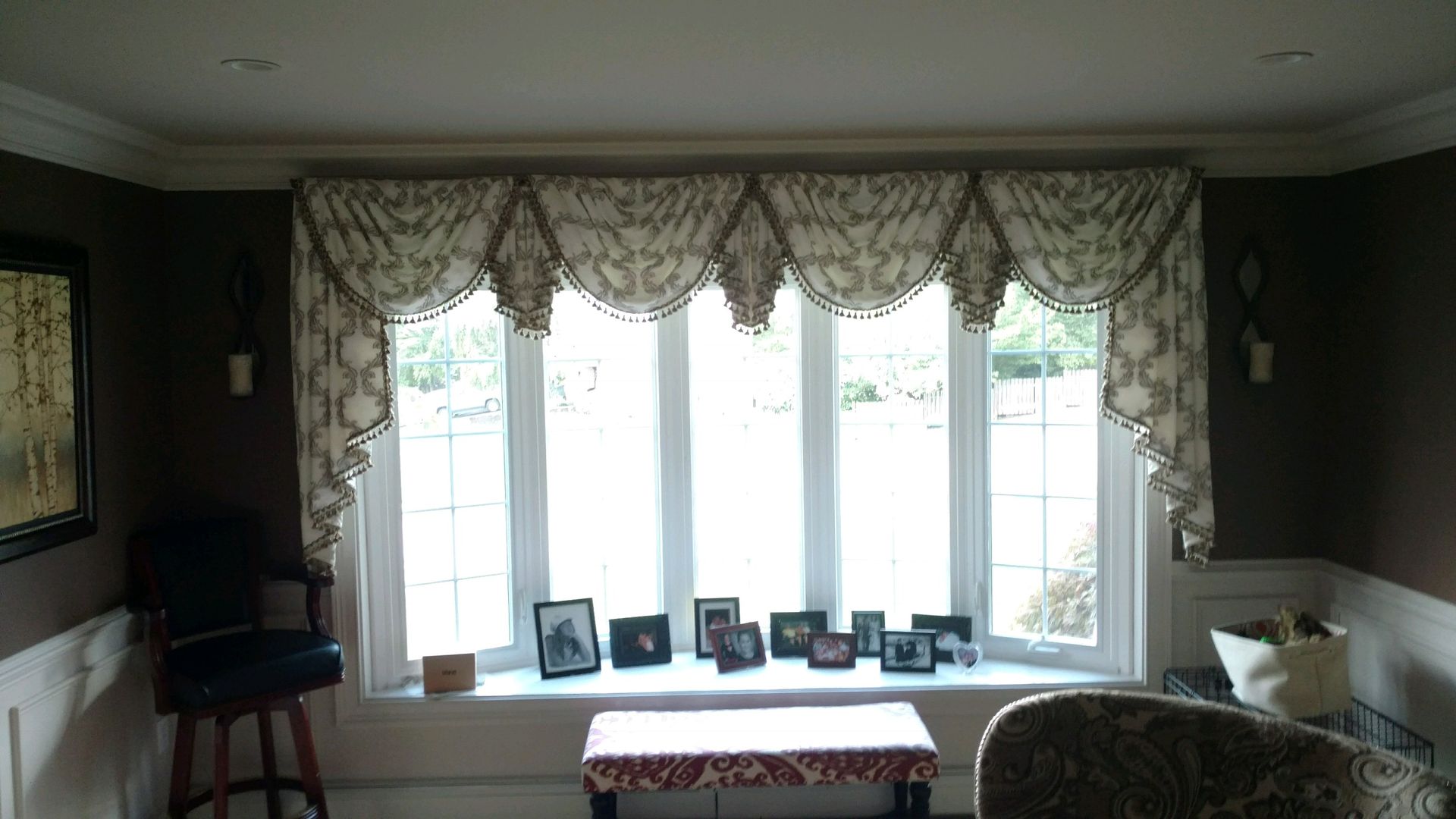 Large bay window with patterned valance, photos on the sill, and dark walls.