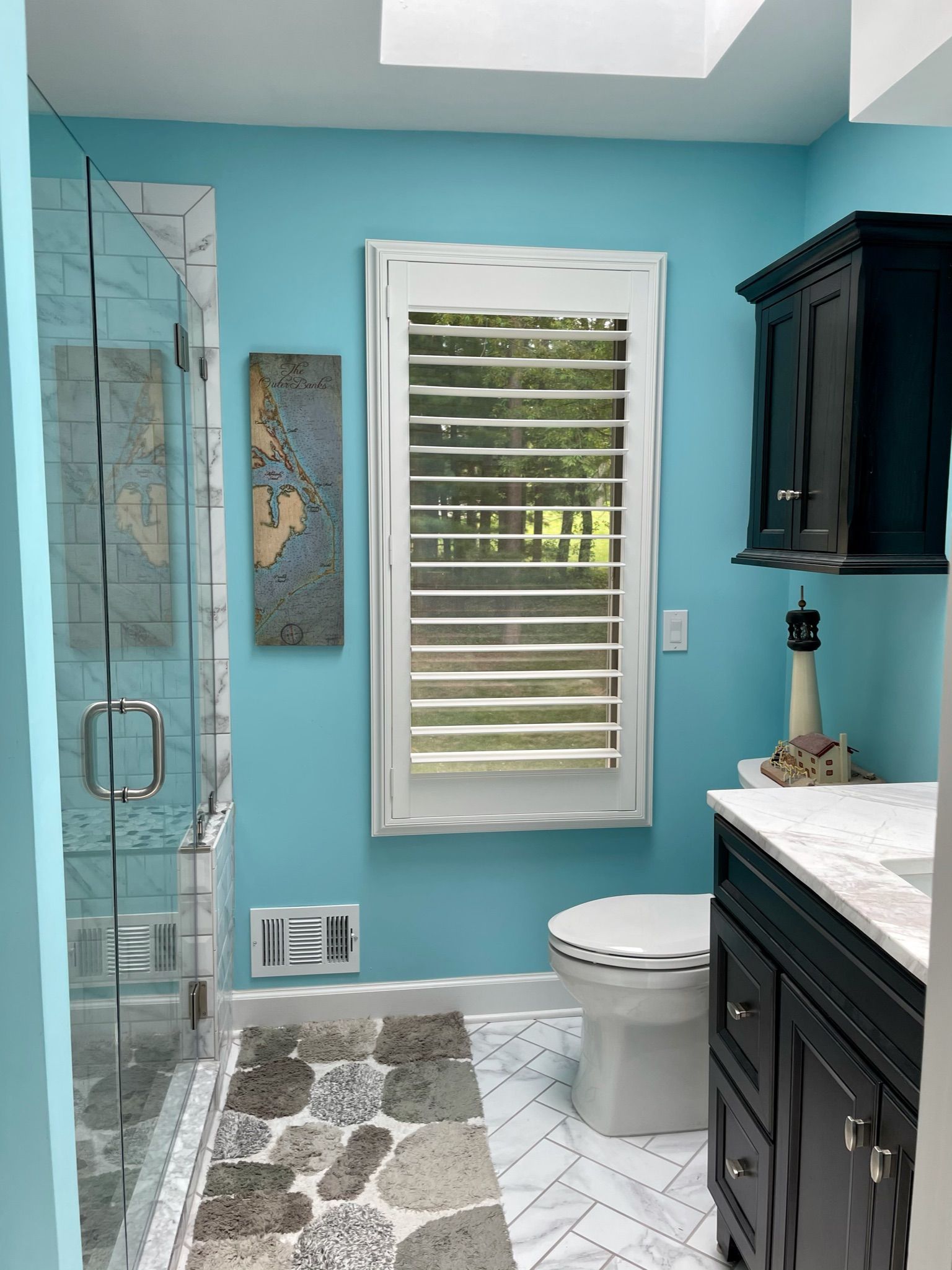 Bathroom with blue walls, glass shower, black vanity, and white shutters.