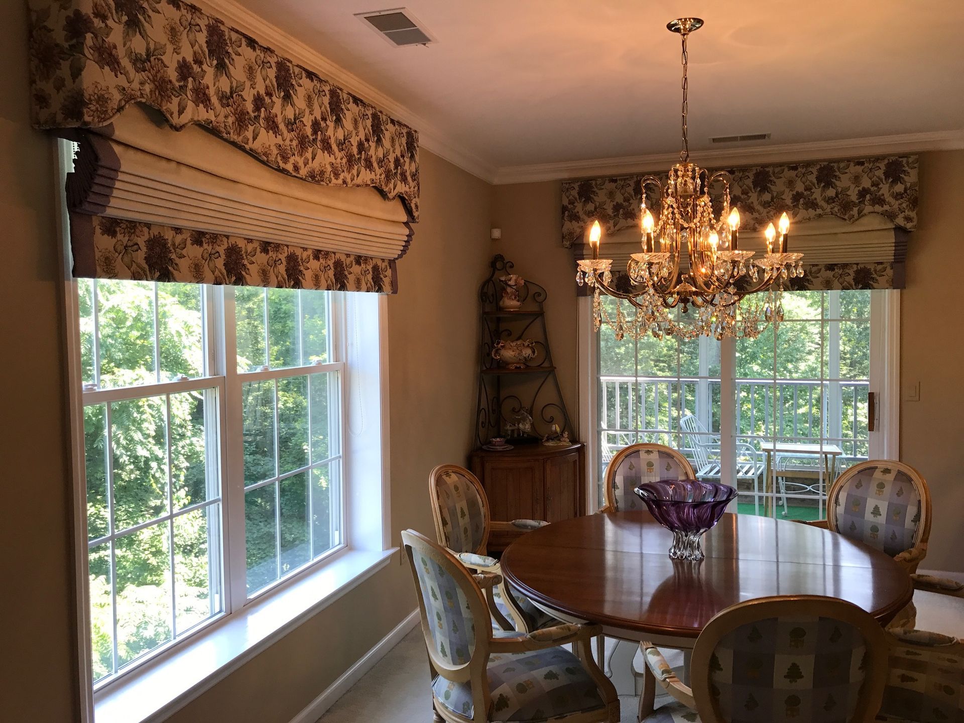 Formal dining room with a round wooden table, patterned chairs, and floral window valances.