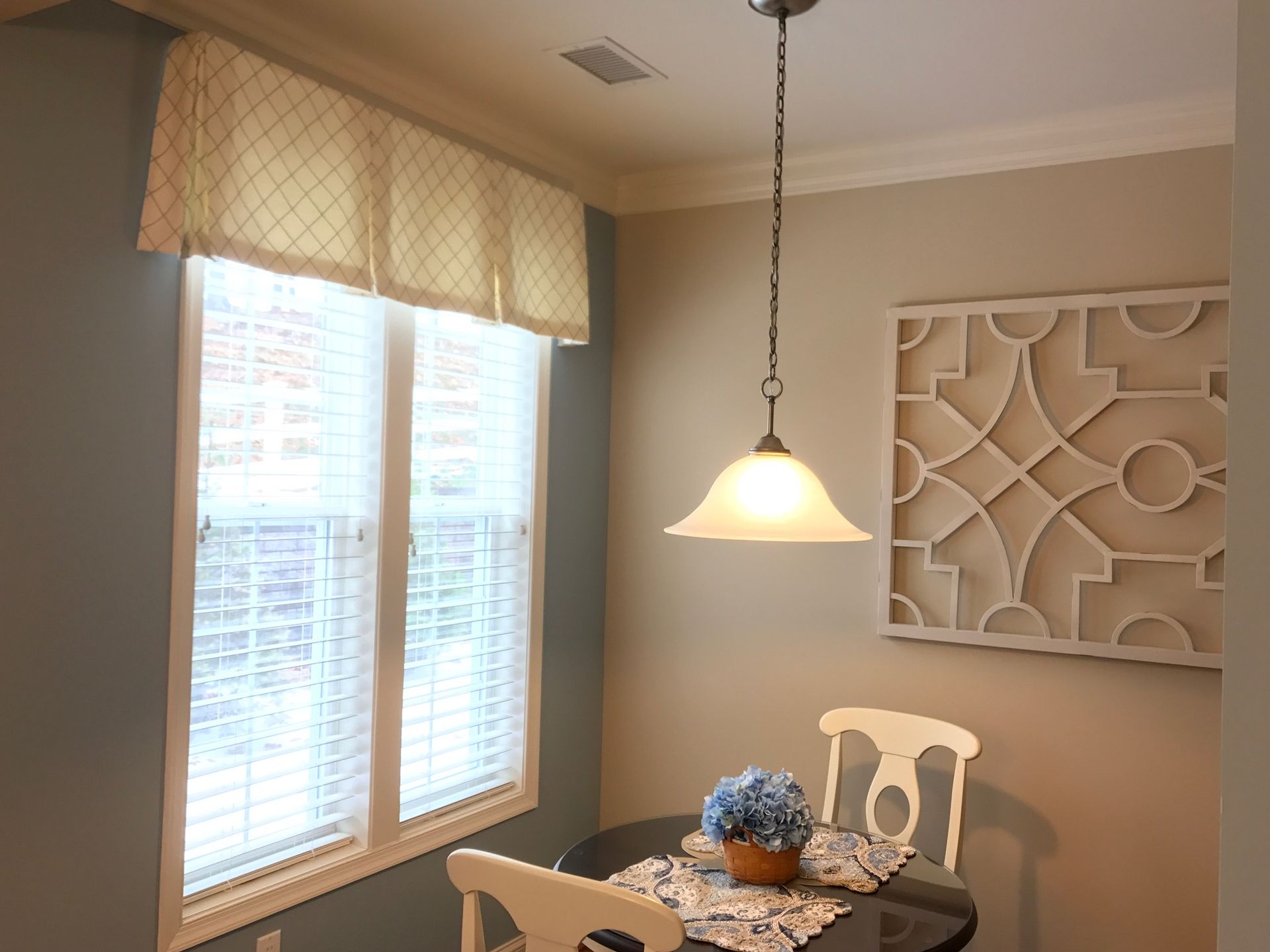 Small dining area with a window, light fixture, table set for two, and decorative wall art.