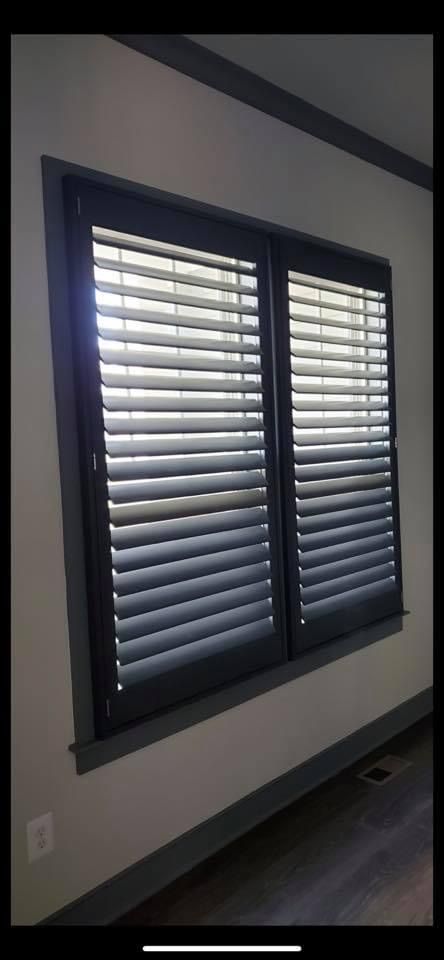 A window with closed, black shutters in a room with gray walls and dark trim.