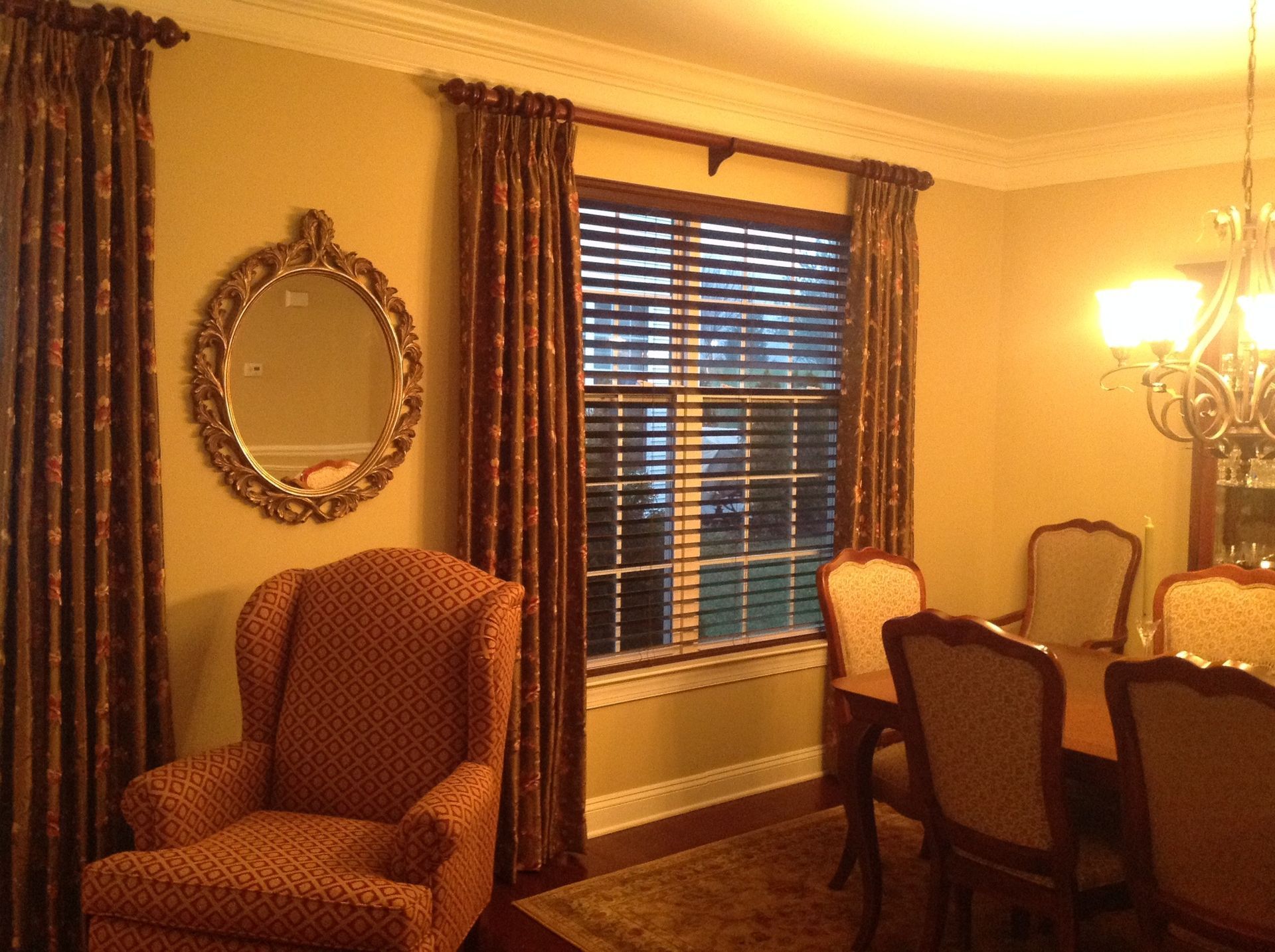 Formal dining room with ornate mirror, patterned curtains, wingback chair, and dining table.