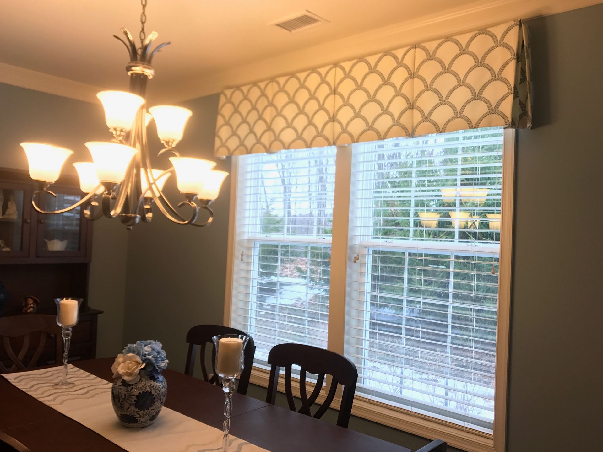 Dining room with patterned valance over a window. A chandelier and dark wood table are present.