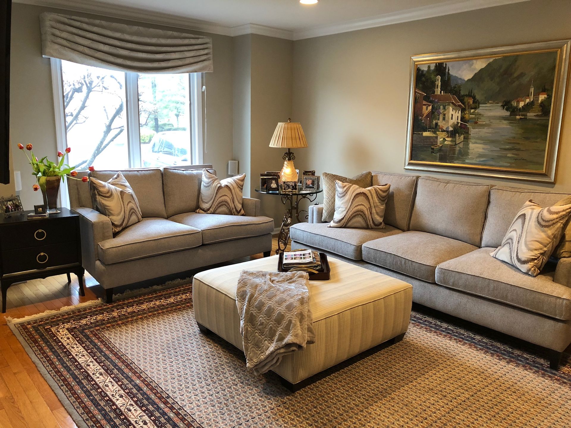 Living room with beige couches, large ottoman, artwork, and a patterned rug.