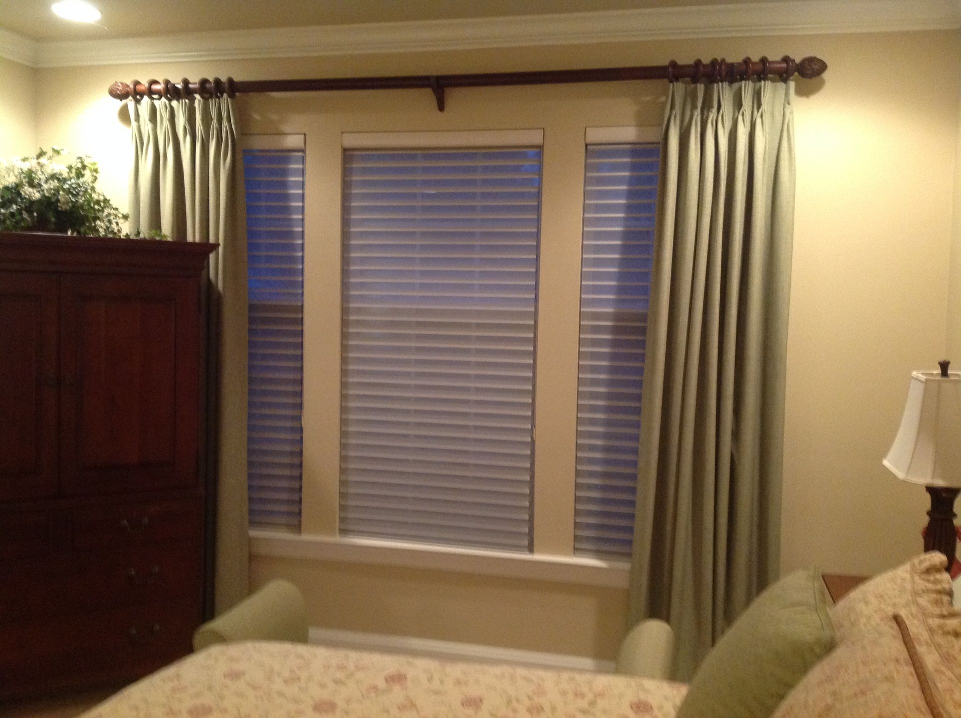 Bedroom window with light green curtains, brown wooden rod, and cream walls.