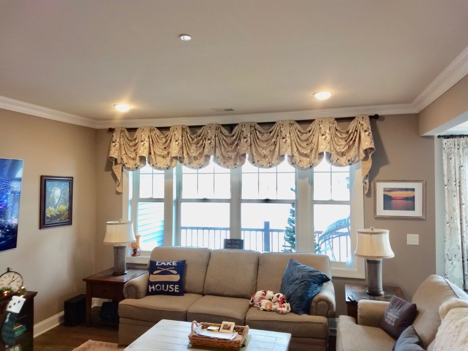 Living room with beige walls, sofa under window with patterned valance, end tables with lamps.