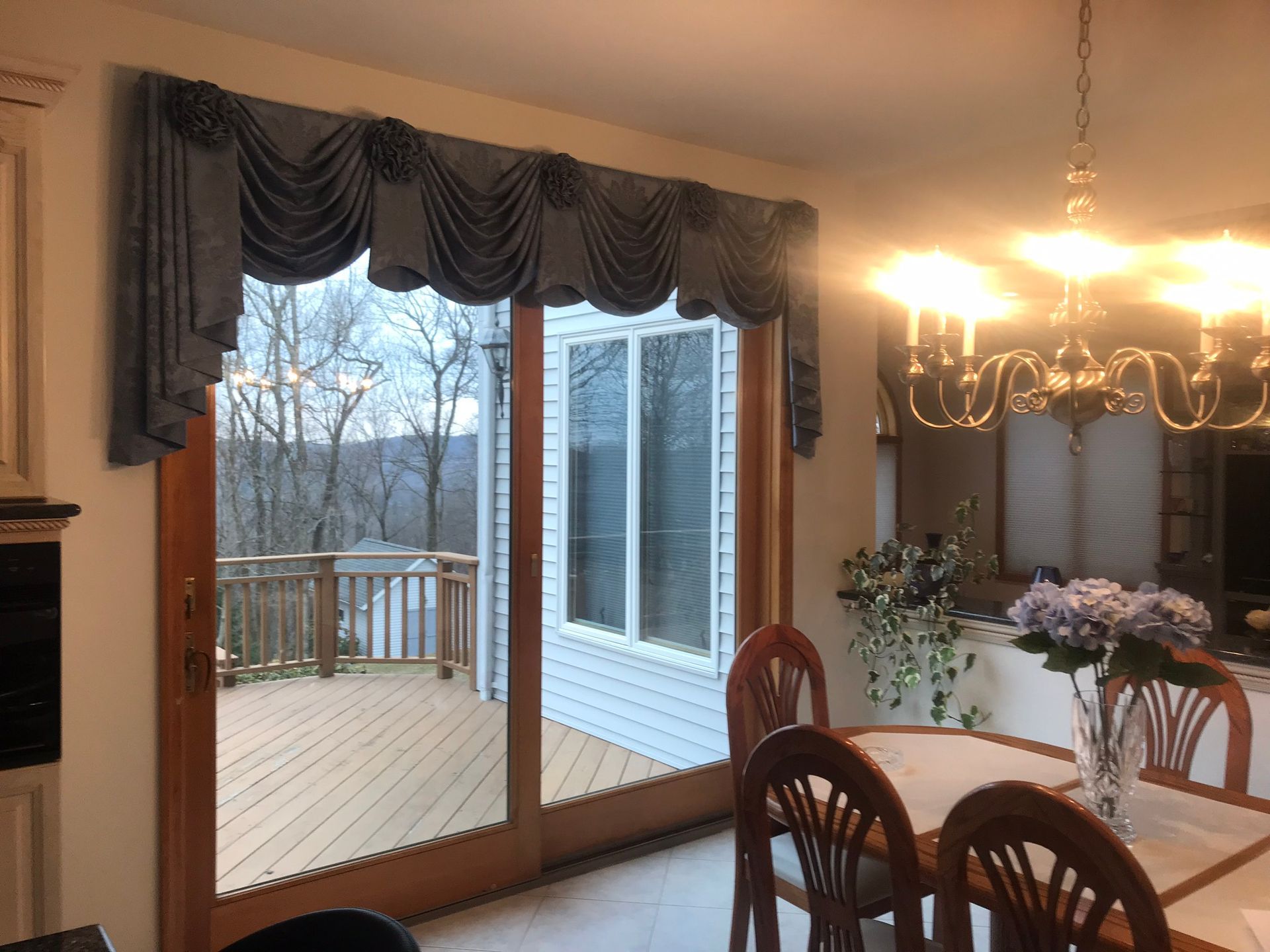 Sliding glass doors open onto a deck with blue valance. Dining area with chandelier and table.