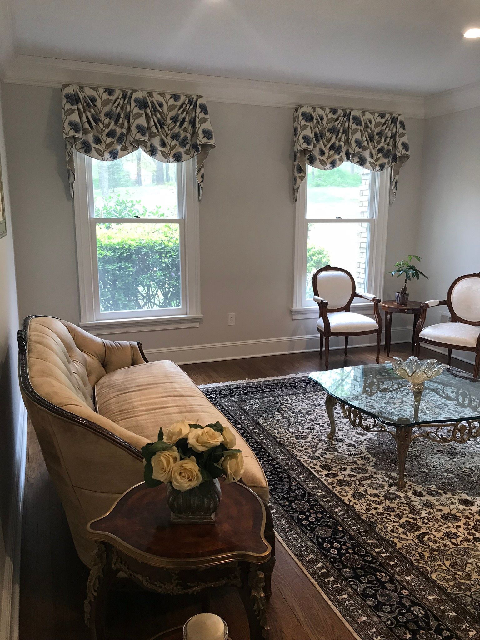 Elegant living room with floral valances, sofa, chairs, and patterned rug.