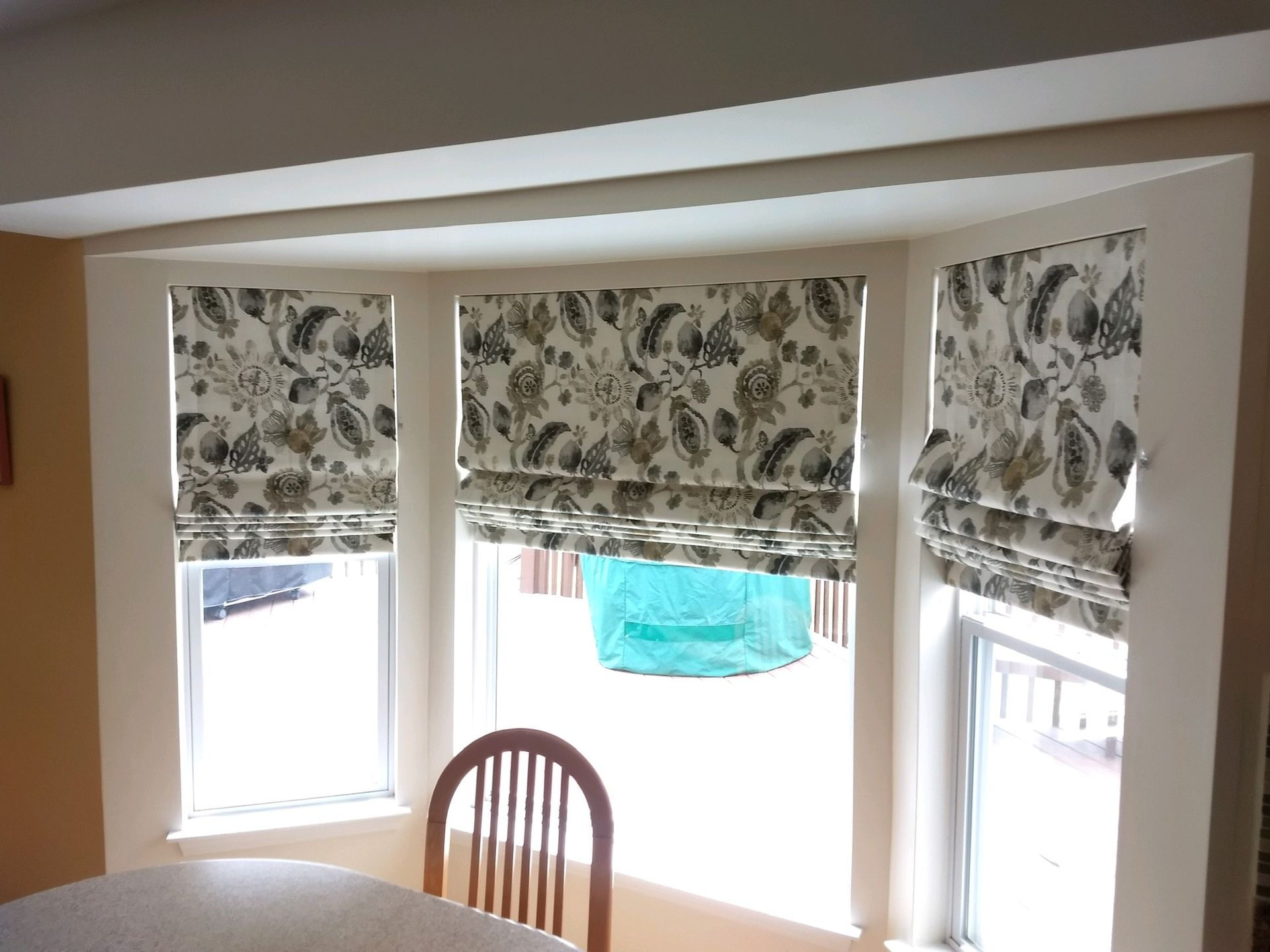 Bay window with floral Roman shades; a wooden chair sits in front of the window.