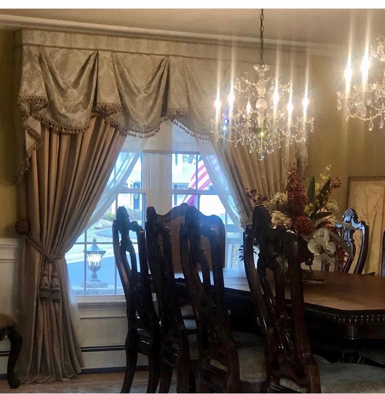 Dining room with draped curtains, chandelier, wooden chairs, and a dining table.