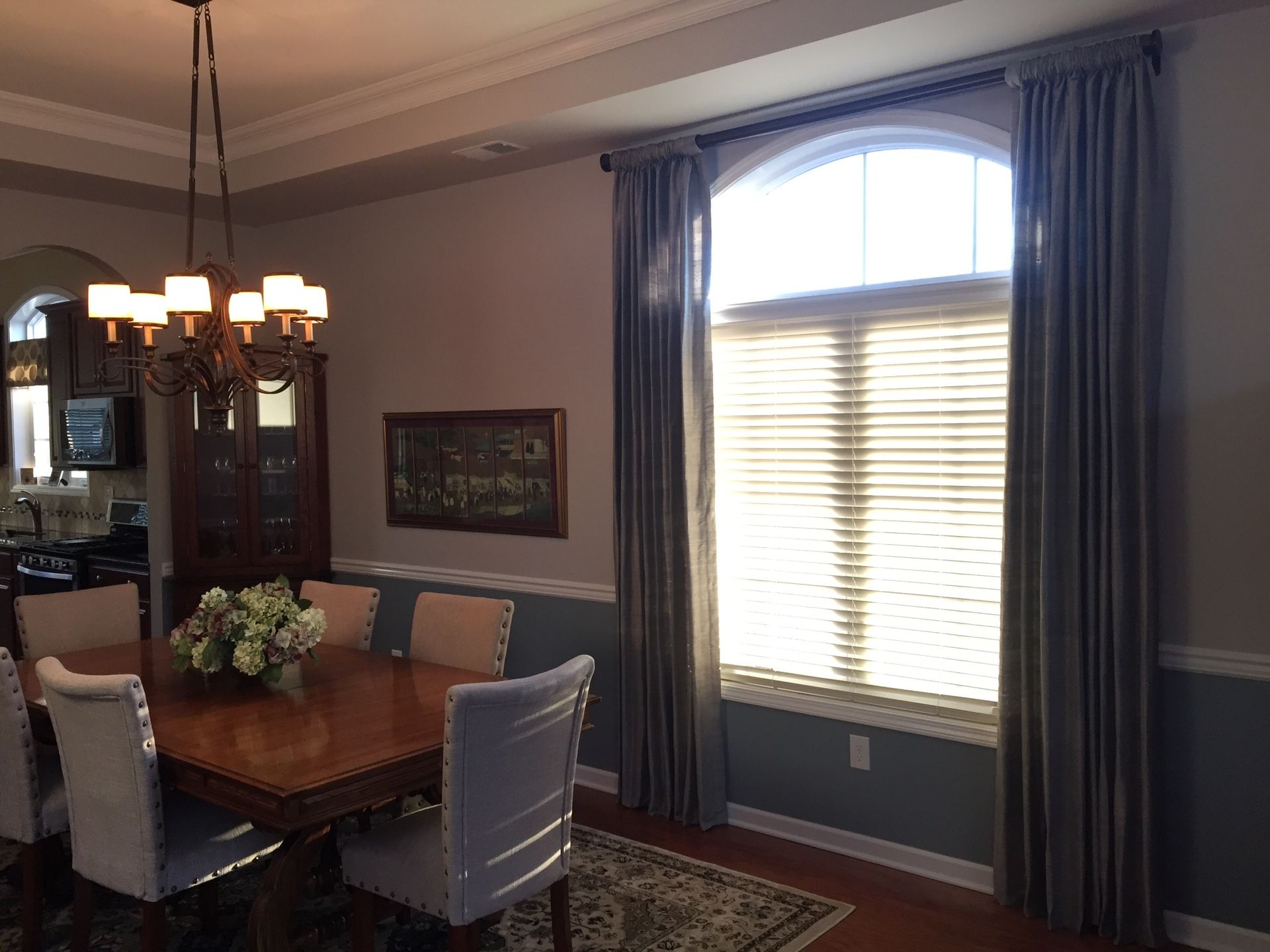 Formal dining room with a large arched window, gray curtains, and a wooden dining table set for a meal.