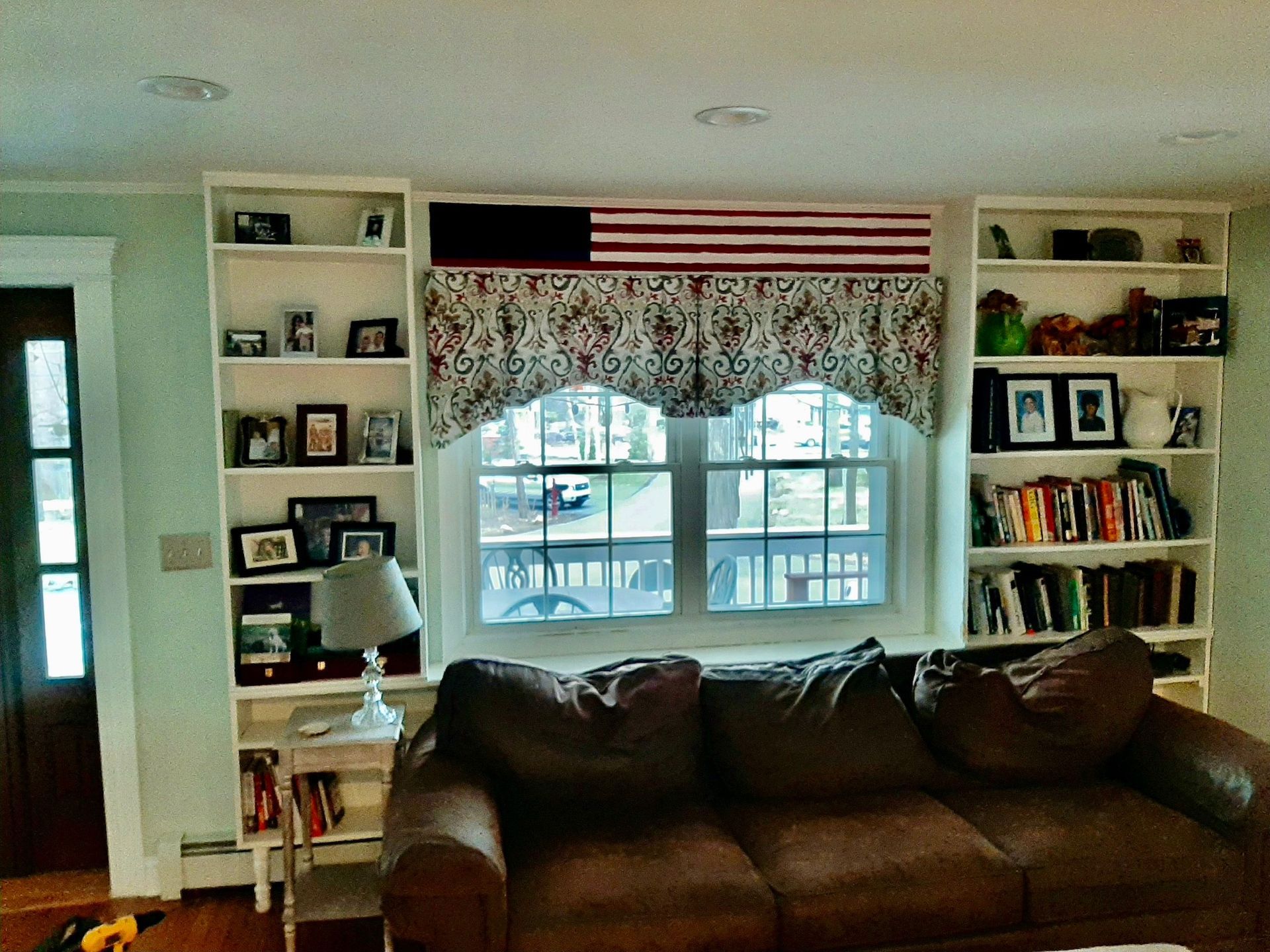 Living room with built-in bookshelves flanking a window. A brown sofa sits in front of the window.