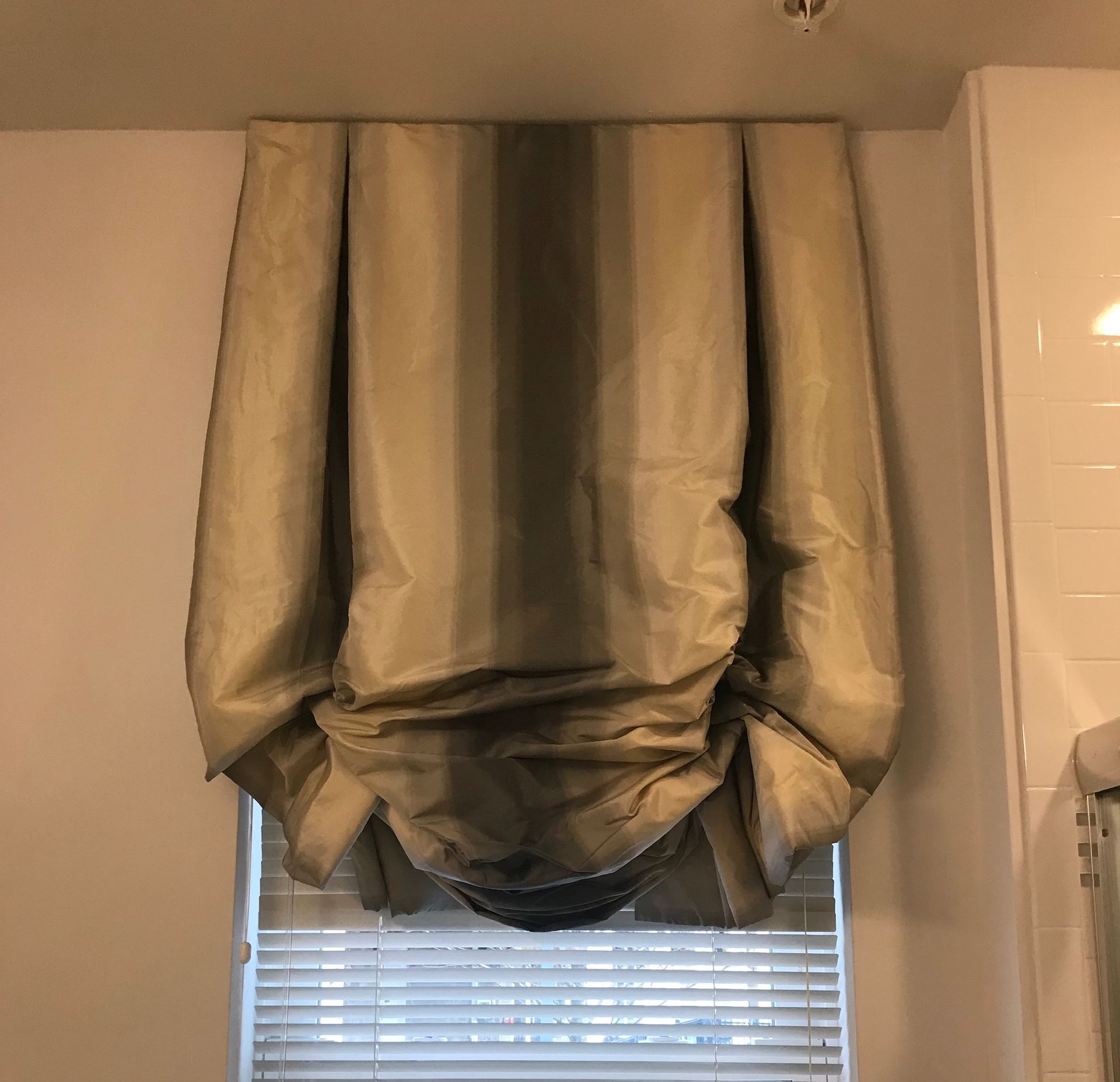 Roman shade in beige and brown stripes over a window with blinds.