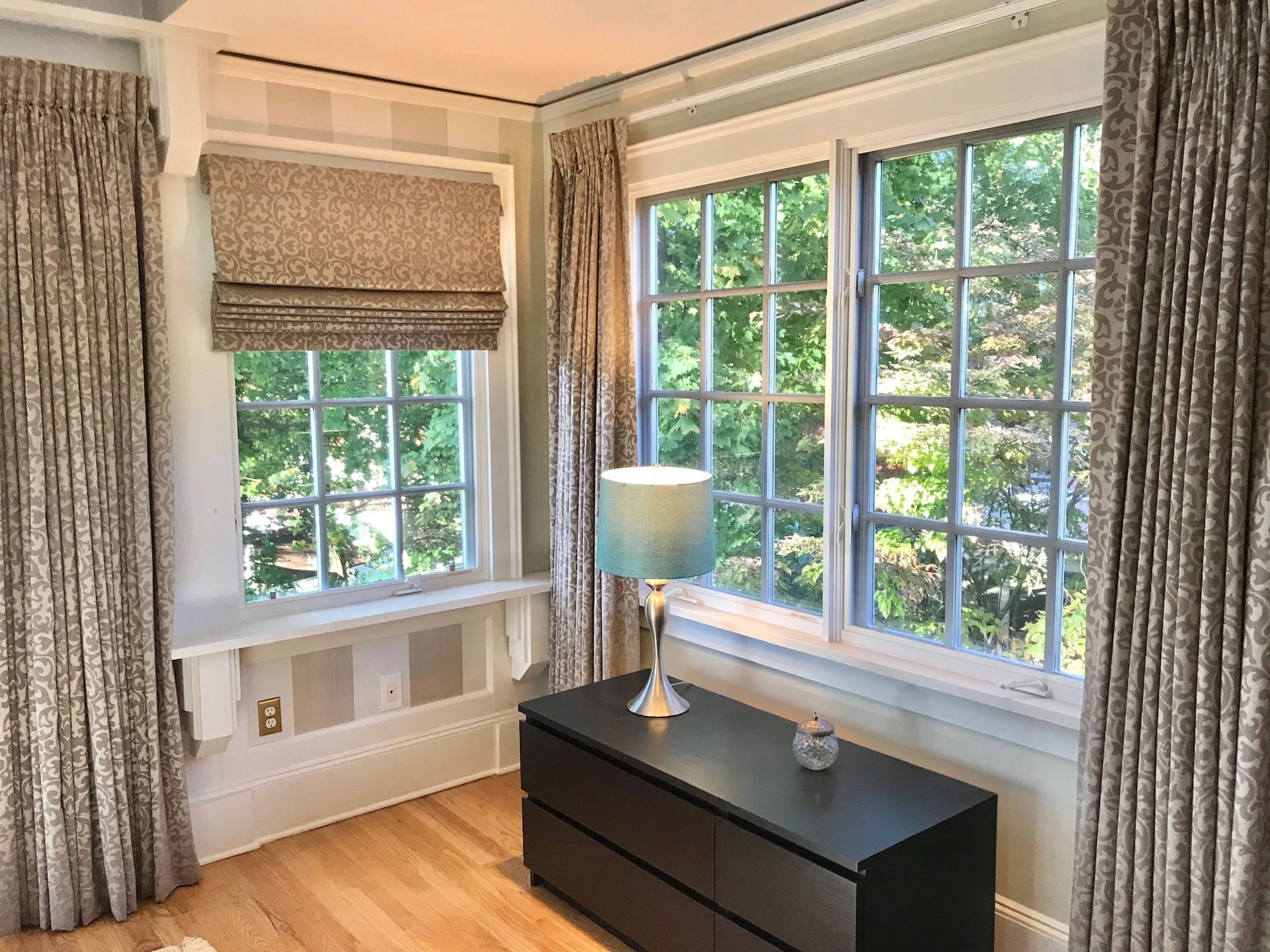 Room with windows, curtains, and a dresser. Beige and green tones.