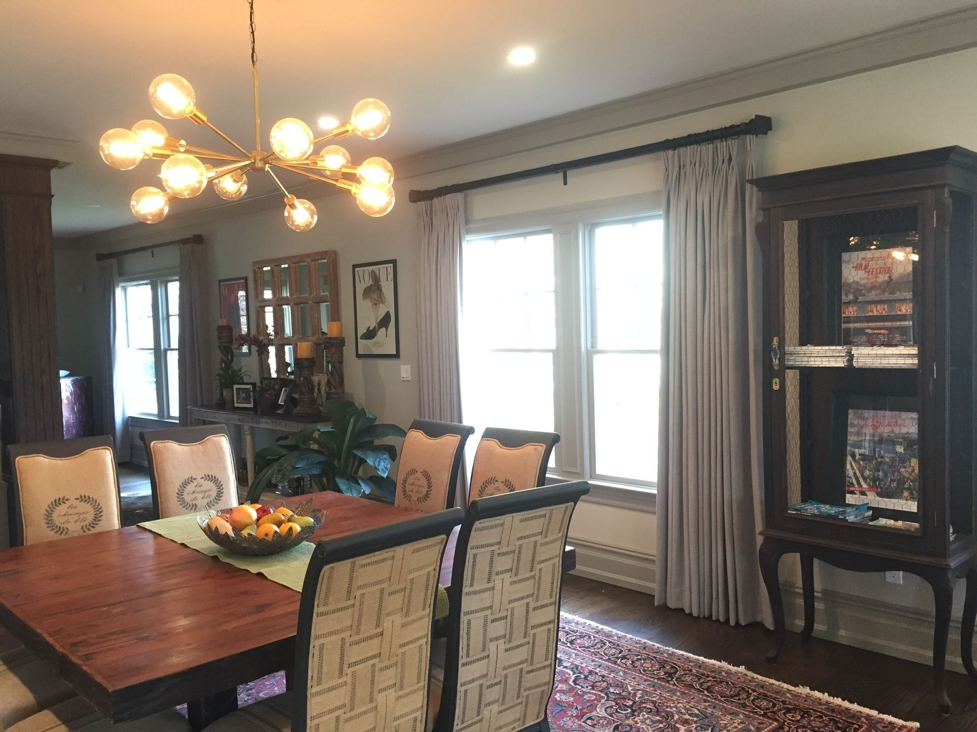 Dining room with a dark wood table, chairs, and a glass display cabinet; soft gray curtains.