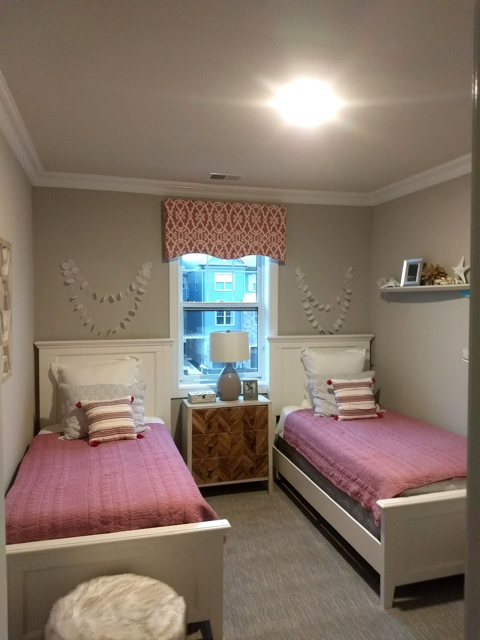 Two twin beds in a bedroom with matching nightstand, window, pink and white decor.