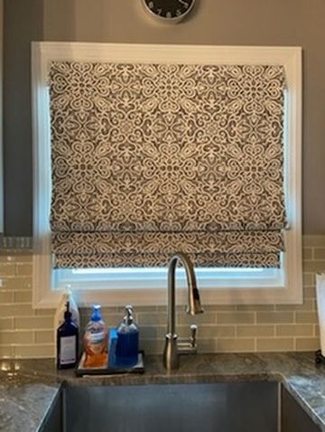 Kitchen window with Roman shade. A stainless steel faucet, sink, and soap bottles are in front of the window.