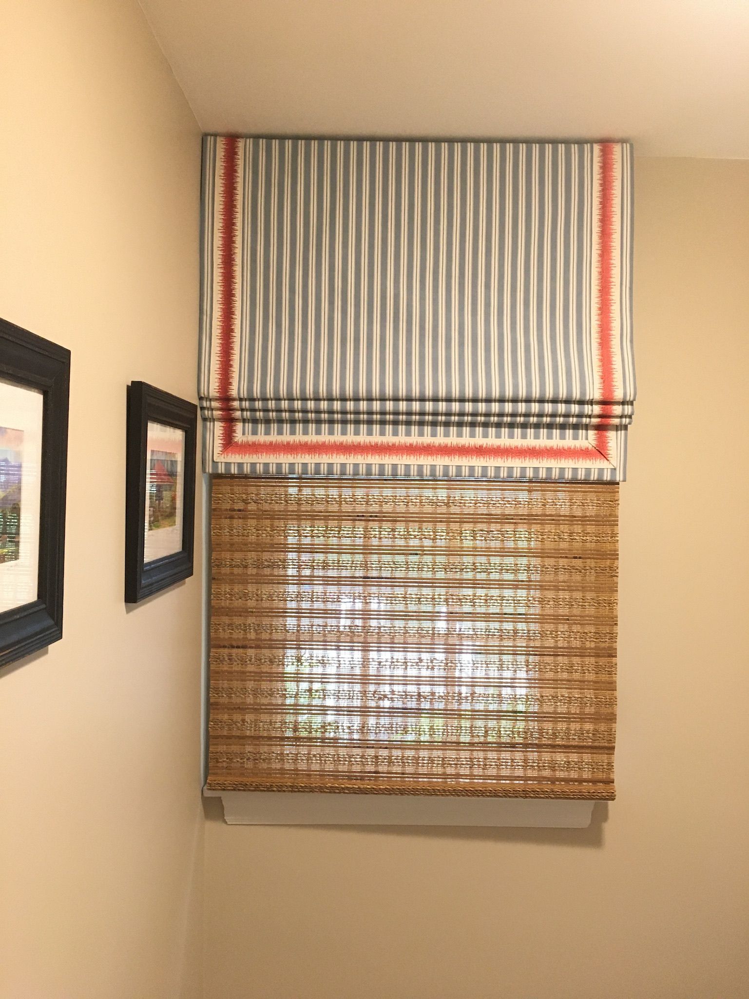 Window with layered blinds: striped gray fabric over bamboo, framed art on wall.
