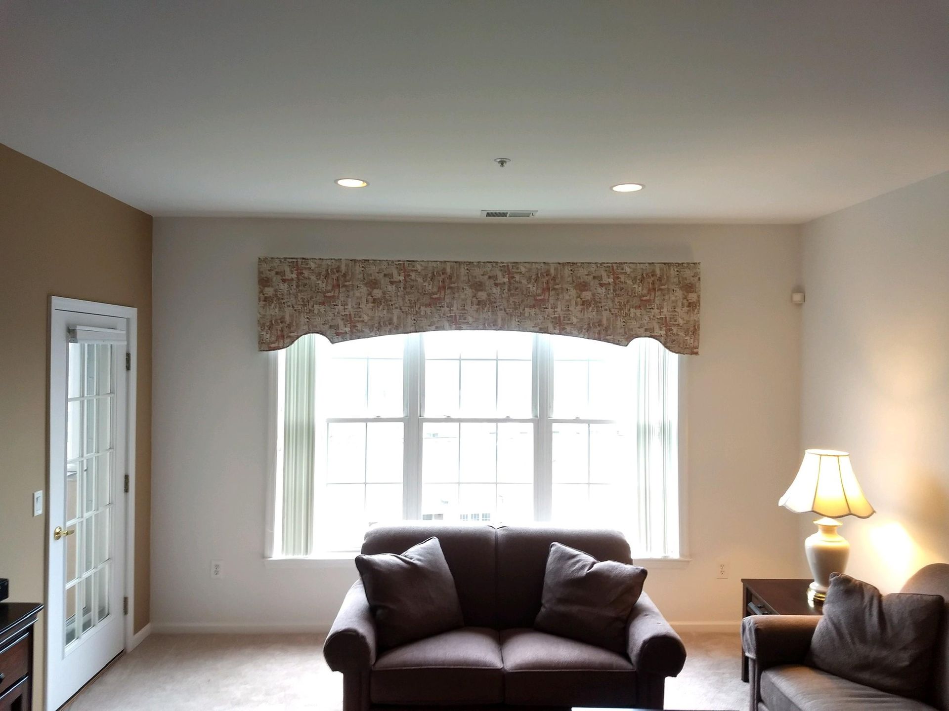 Living room with brown sofa under window with valance and door to the left.