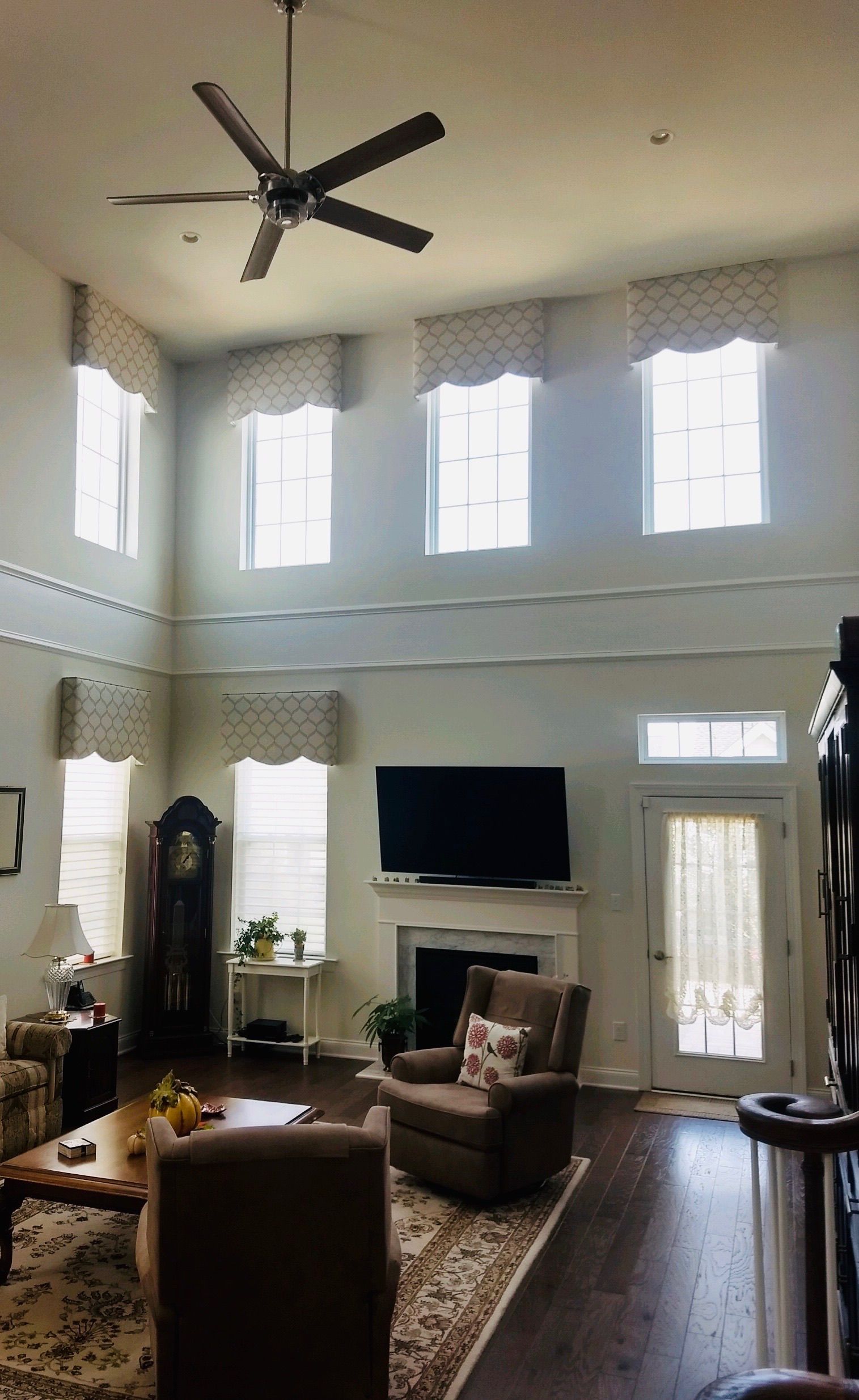 Living room with tall windows, a ceiling fan, fireplace, and a few armchairs.