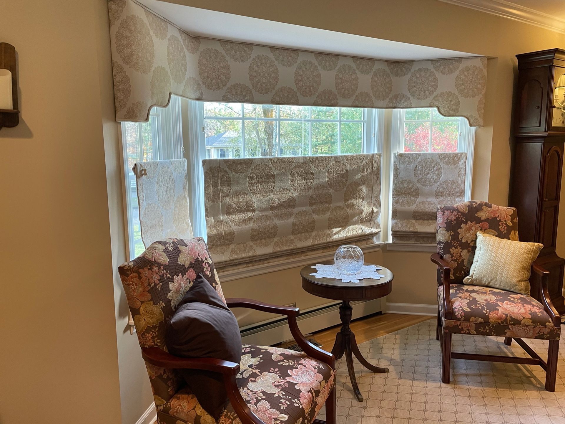 A living room with a bay window, floral chairs, a small table, and brown and beige decor.