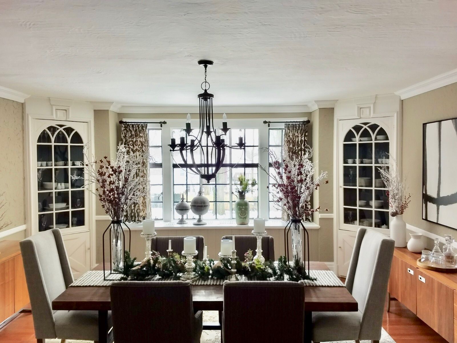 Formal dining room with dark wood table, chandelier, built-in cabinets, and window with floral arrangements.