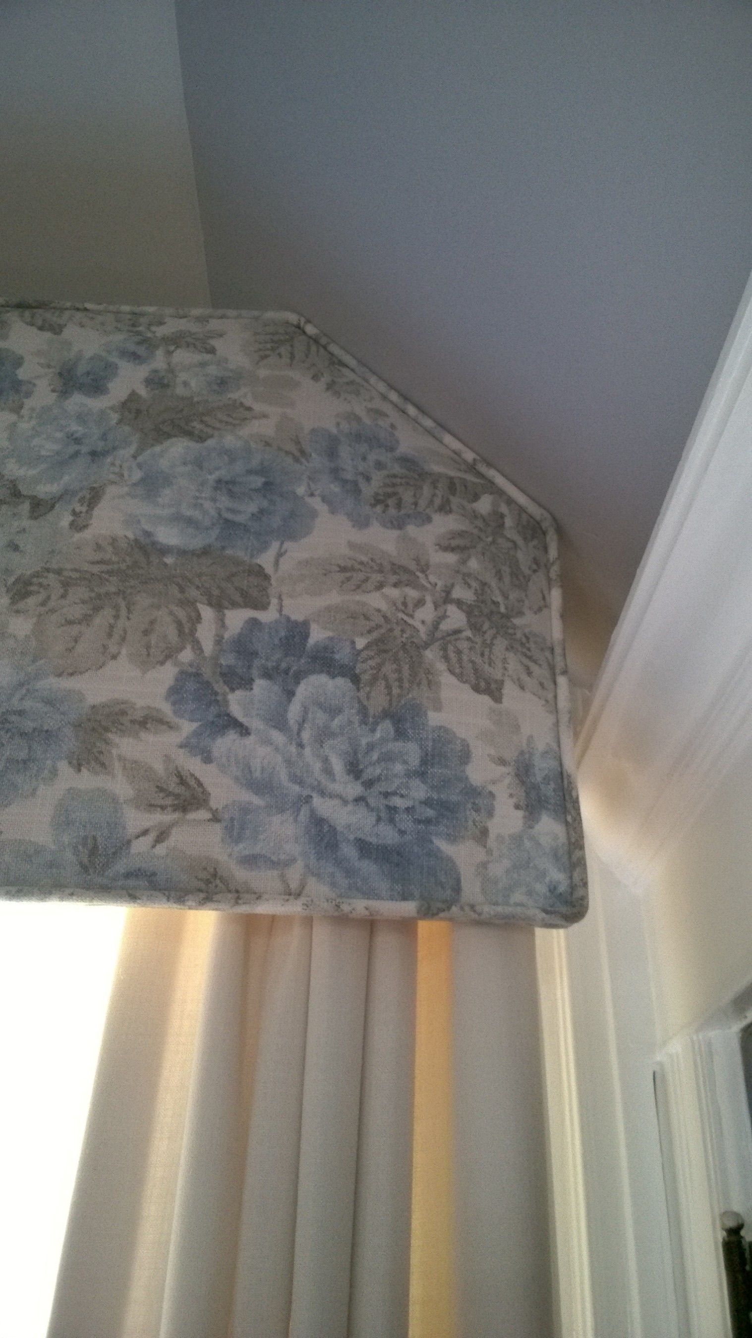 Floral patterned valance over cream-colored curtains, corner of a room.