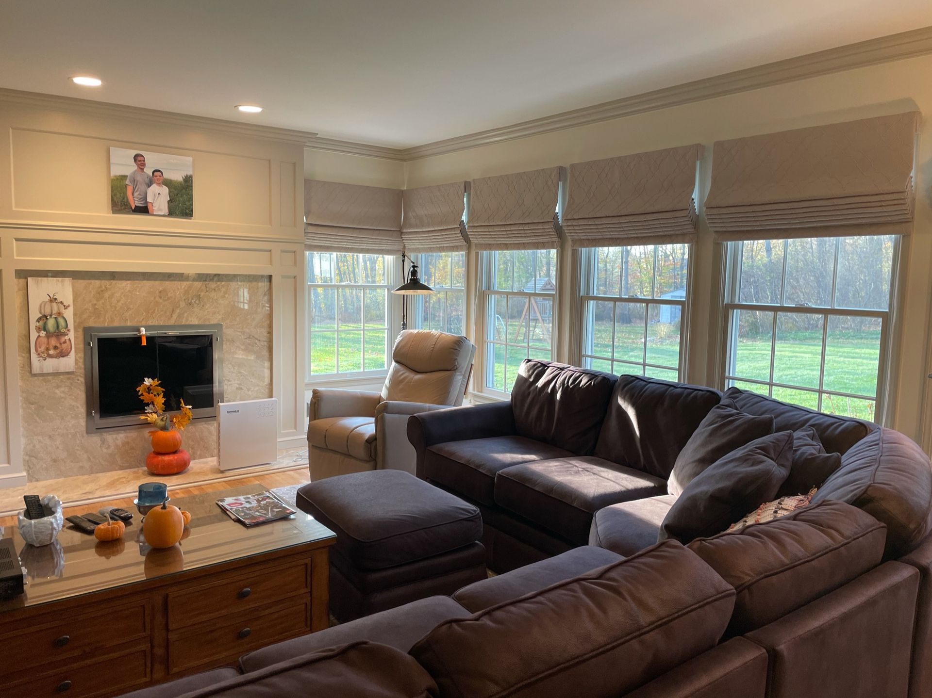 Cozy living room with sectional sofa, fireplace, and large windows with neutral roman shades.