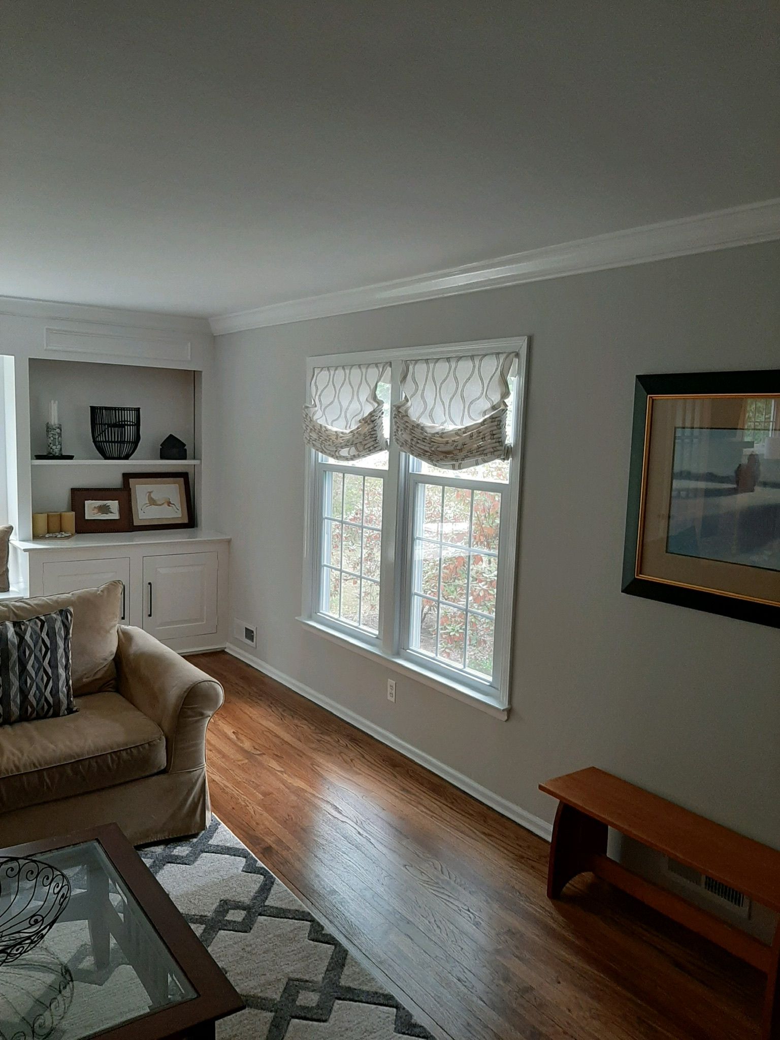 Living room with built-in shelves, windows, and a couch. Wooden floors and a rug.