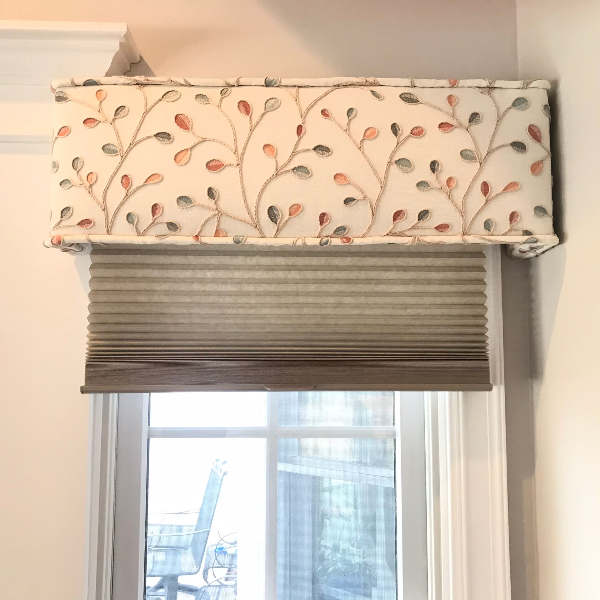 Window with floral valance over pleated shade. White trim, neutral colors.