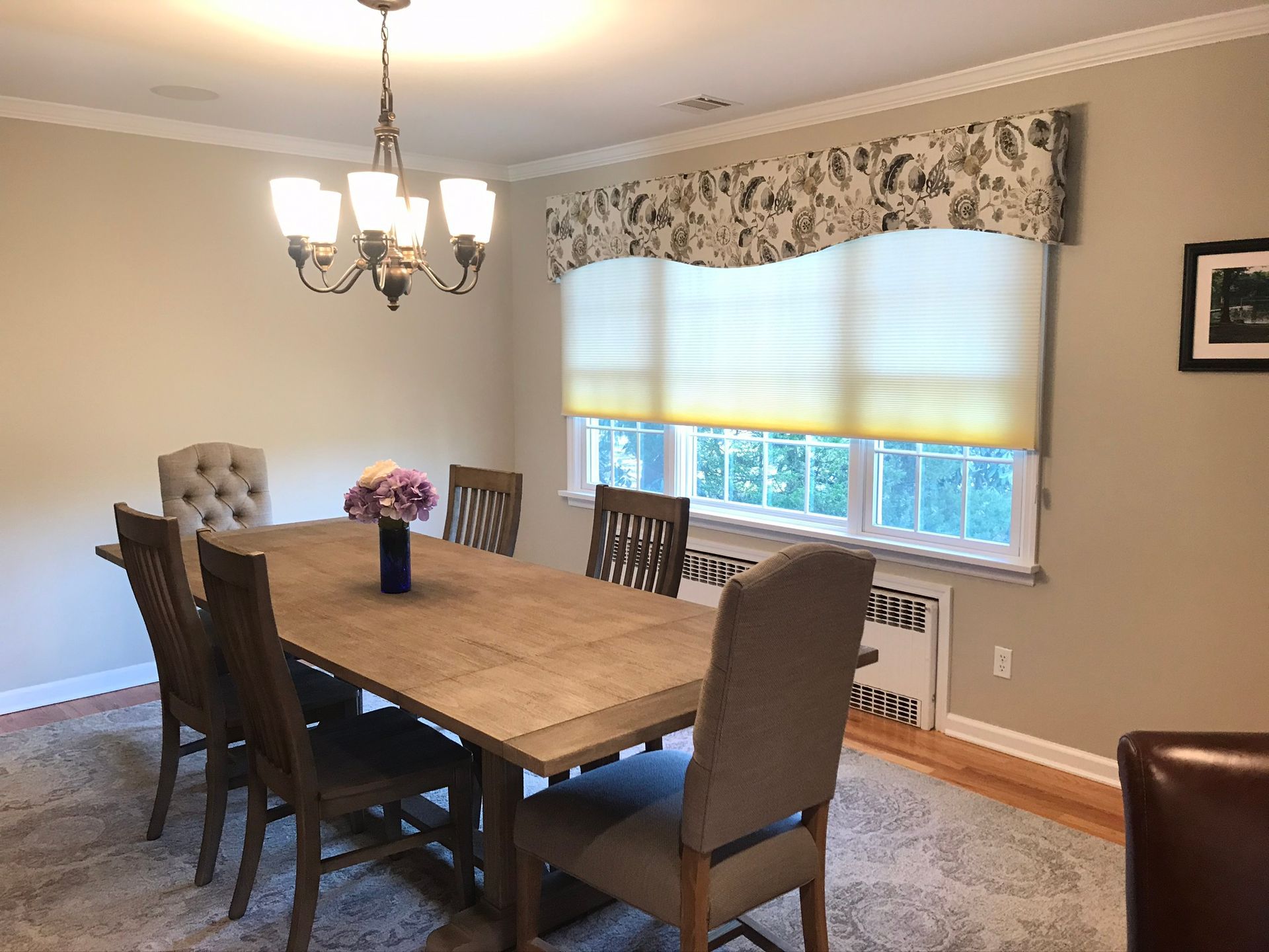 Dining room: wooden table with chairs, chandelier, patterned window treatment, beige walls.