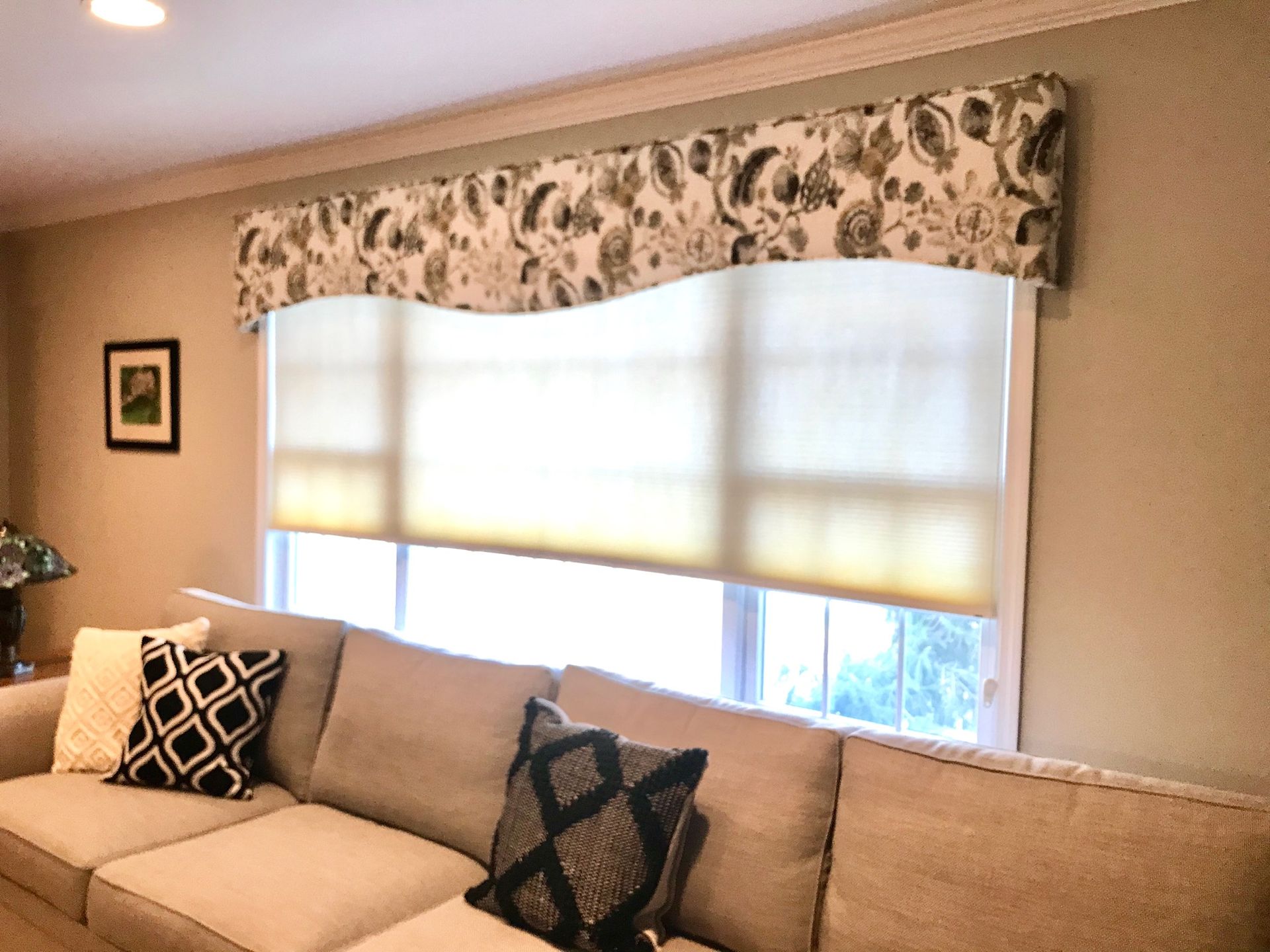 A living room with a beige sofa, window with shades, and decorative valance.