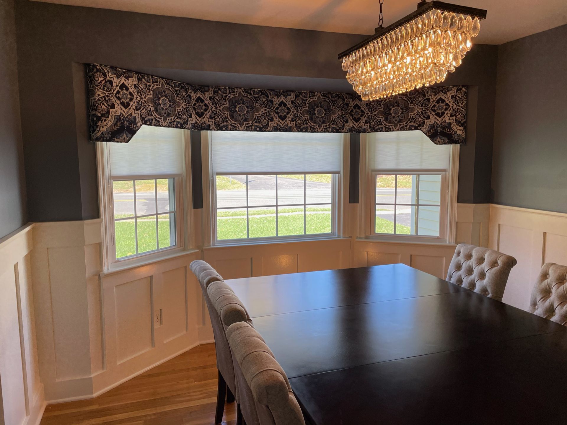 Formal dining room with dark table, tufted chairs, bay windows, and a chandelier.