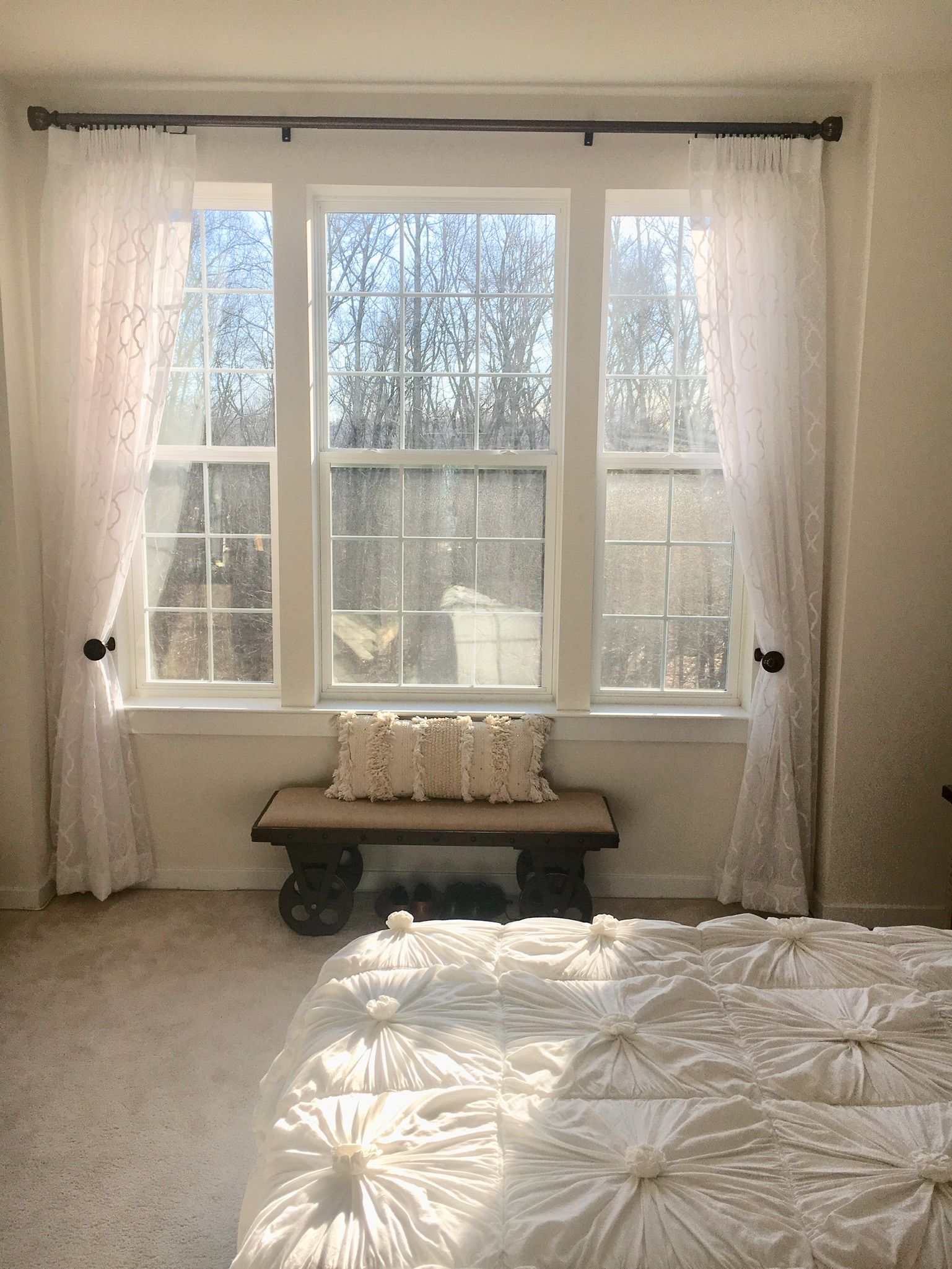 Bedroom with window. White curtains, bench with pillow. Sunlight streams in.