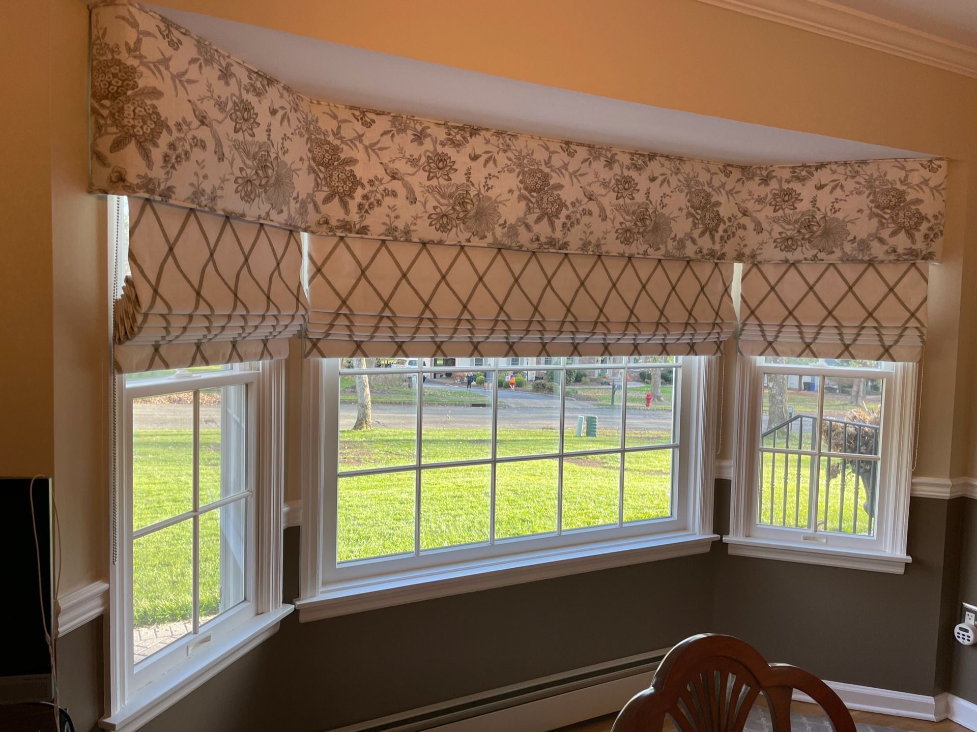Bay window with floral valance and diamond-patterned Roman shades; view of backyard.