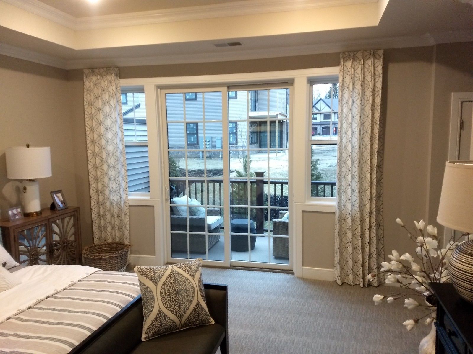 Bedroom with large windows overlooking a patio. Beige and white patterned curtains frame the windows.