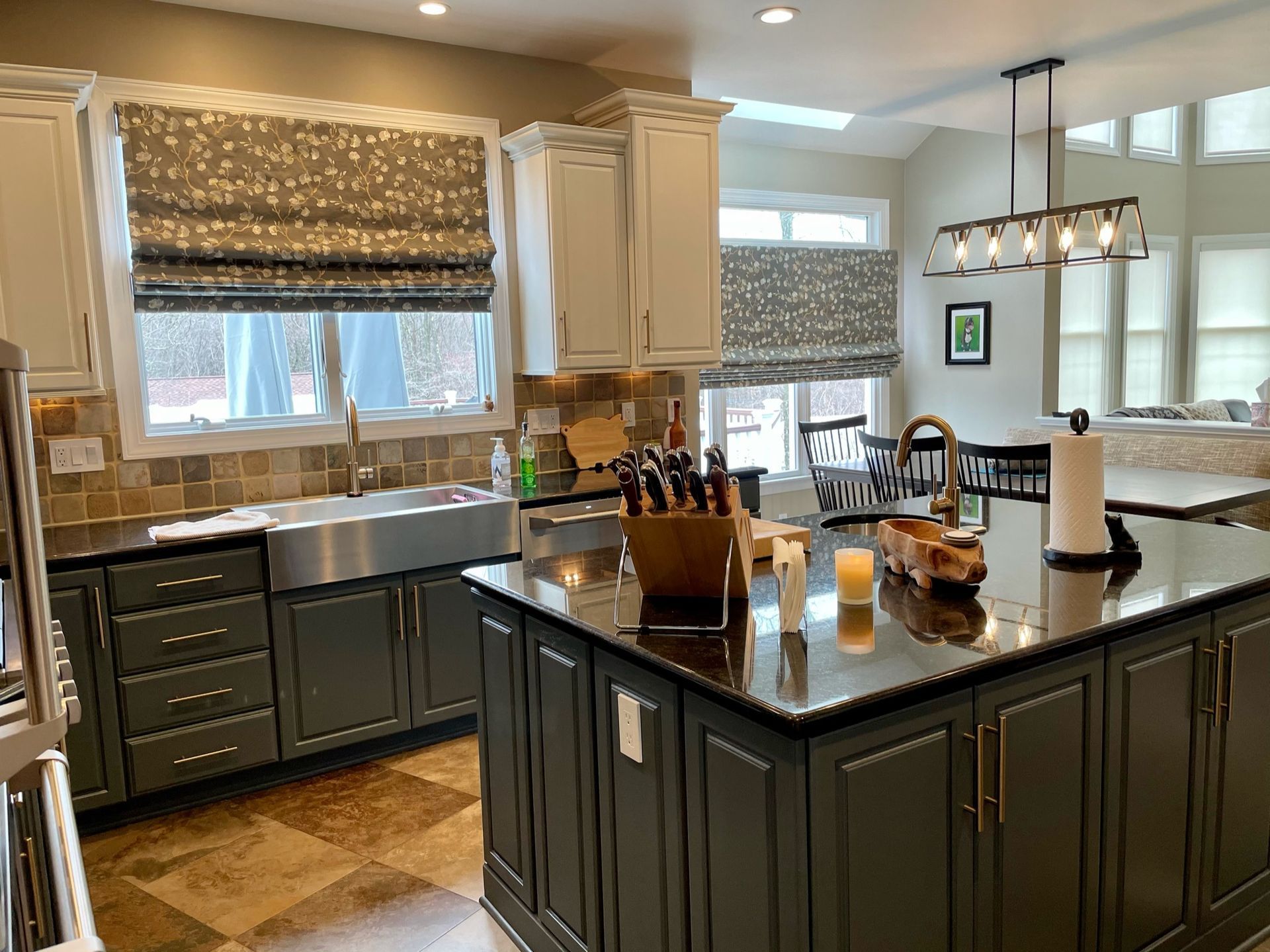 Kitchen with gray and white cabinets, island, stainless steel sink, and patterned window shades.