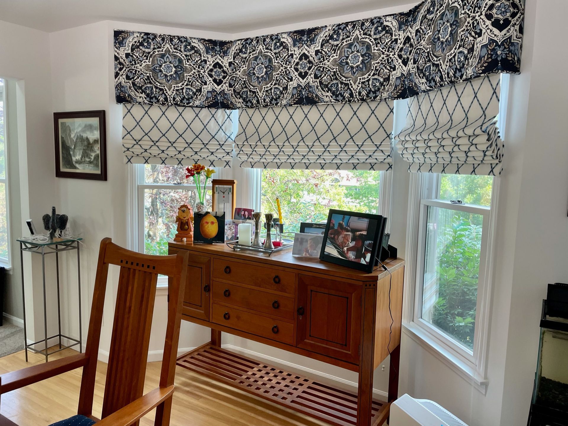 A room with a wooden cabinet in front of windows, framed by matching patterned valance and roman shades.