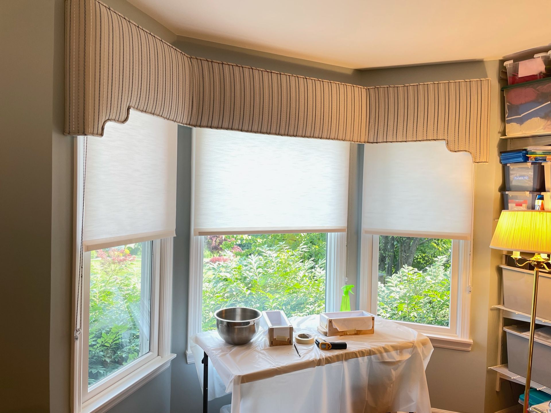 Bay window with white honeycomb blinds and a decorative valance; workspace in front.
